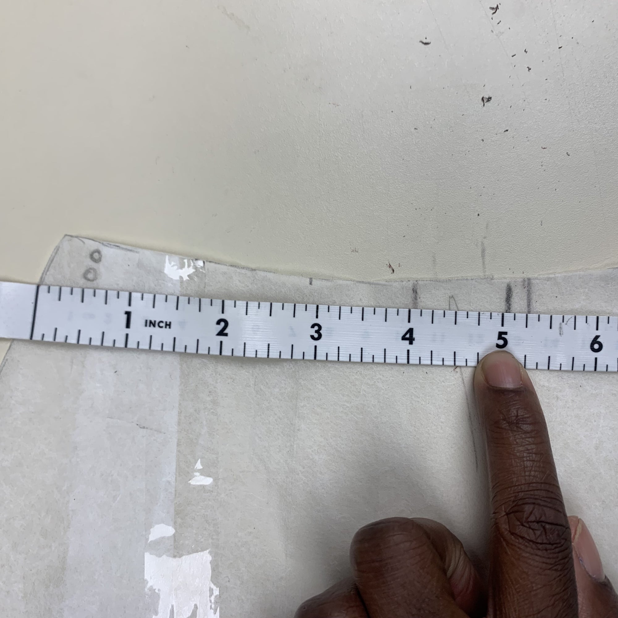 A tape measure, measuring 5 inches from the side of the back B pieces in towards the center back. On fabric tracing paper on a beige background.
