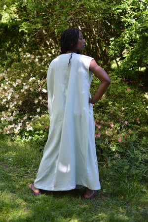 Back of African American woman standing with hang on her hip with greenery in the background.