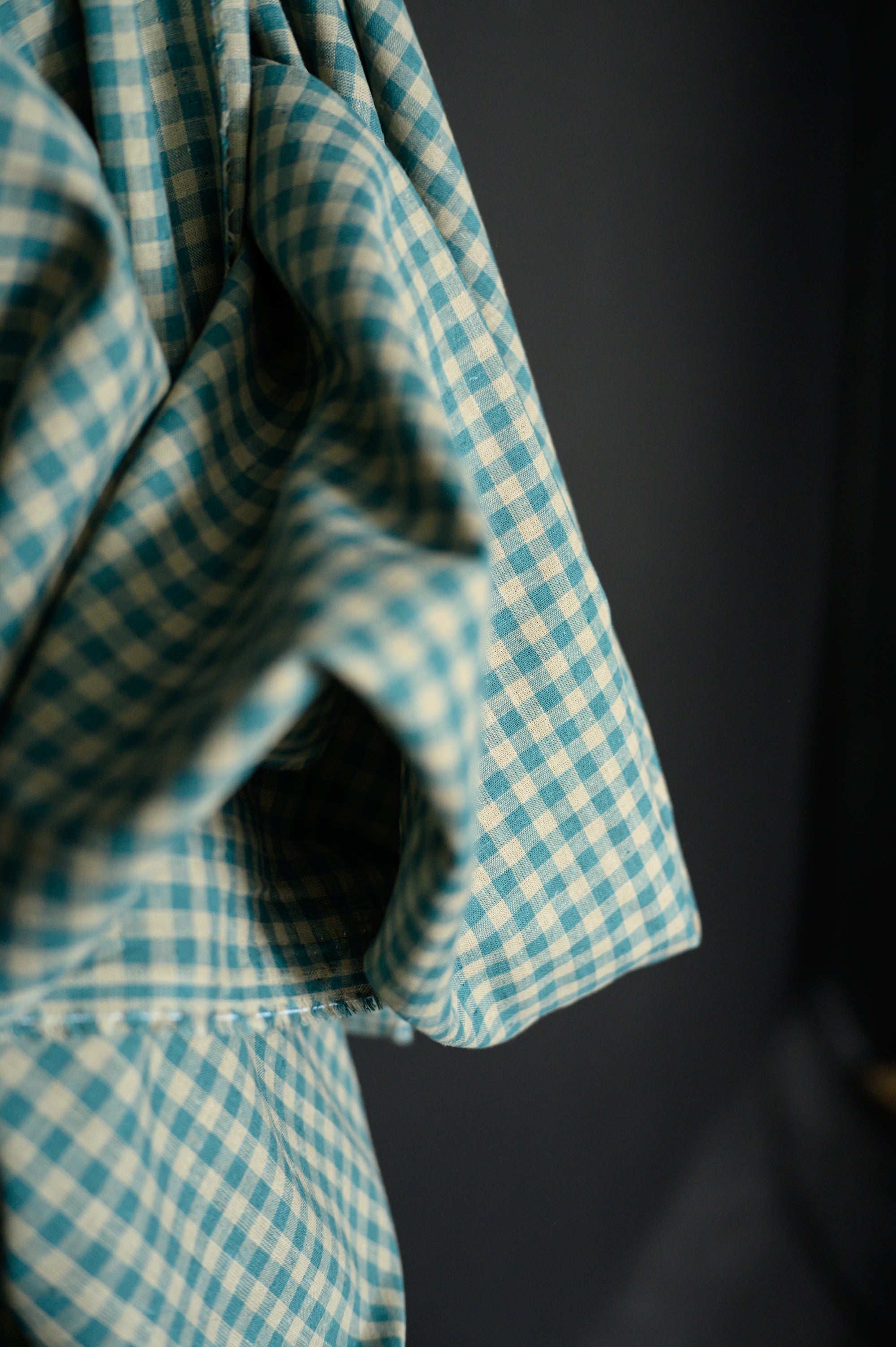 Close up of Teal and tan gingham, cotton/linen blend on a dark grey background.