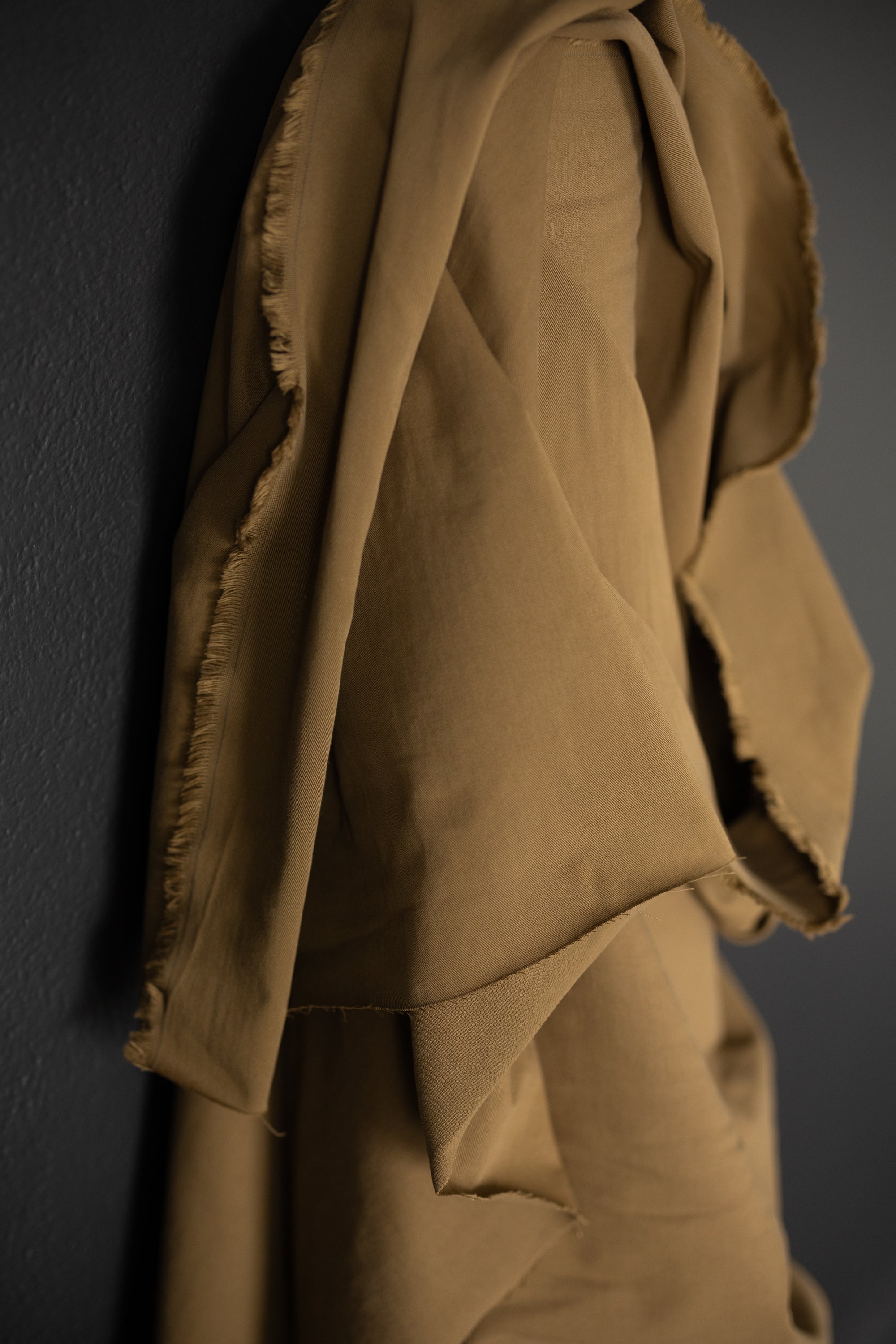 roll of Olive Tan sanded cotton twill fabric on a dark grey background.