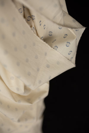 close up ecru with navy polka dots indian cotton fabric on a black background.