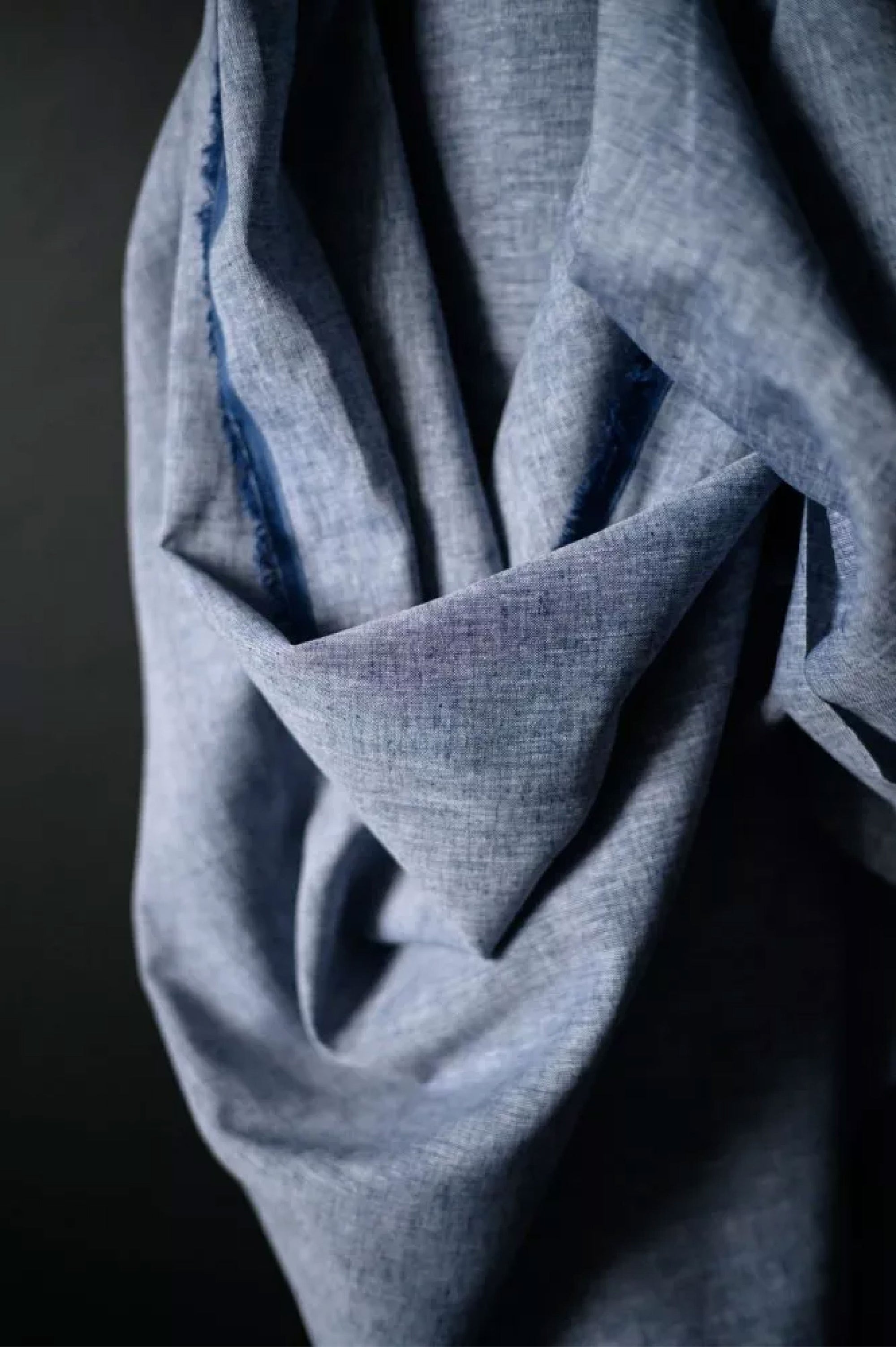 A roll of classic denim bright blue chambray on a dark navy background.