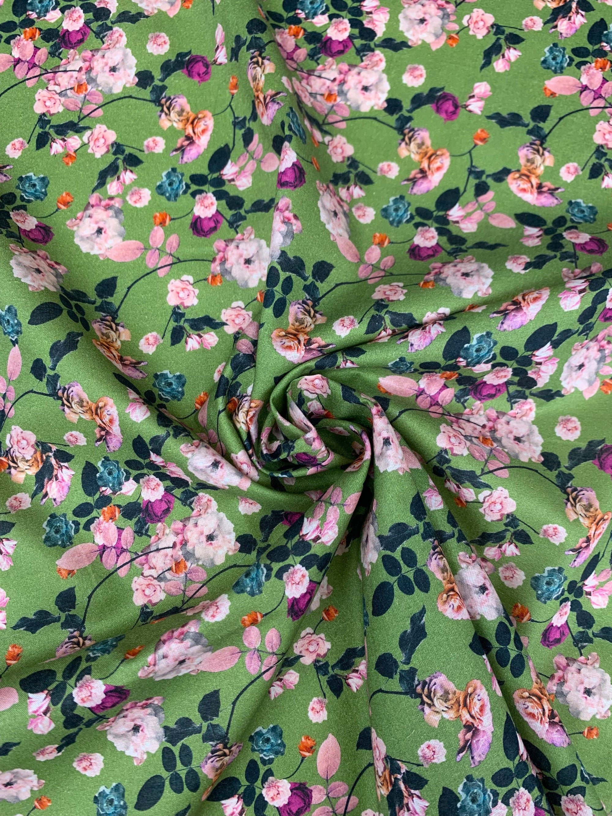 cotton lawn with pink and purple flowers  on a background of green.  With a measuring tape on the bottom of the fabric.