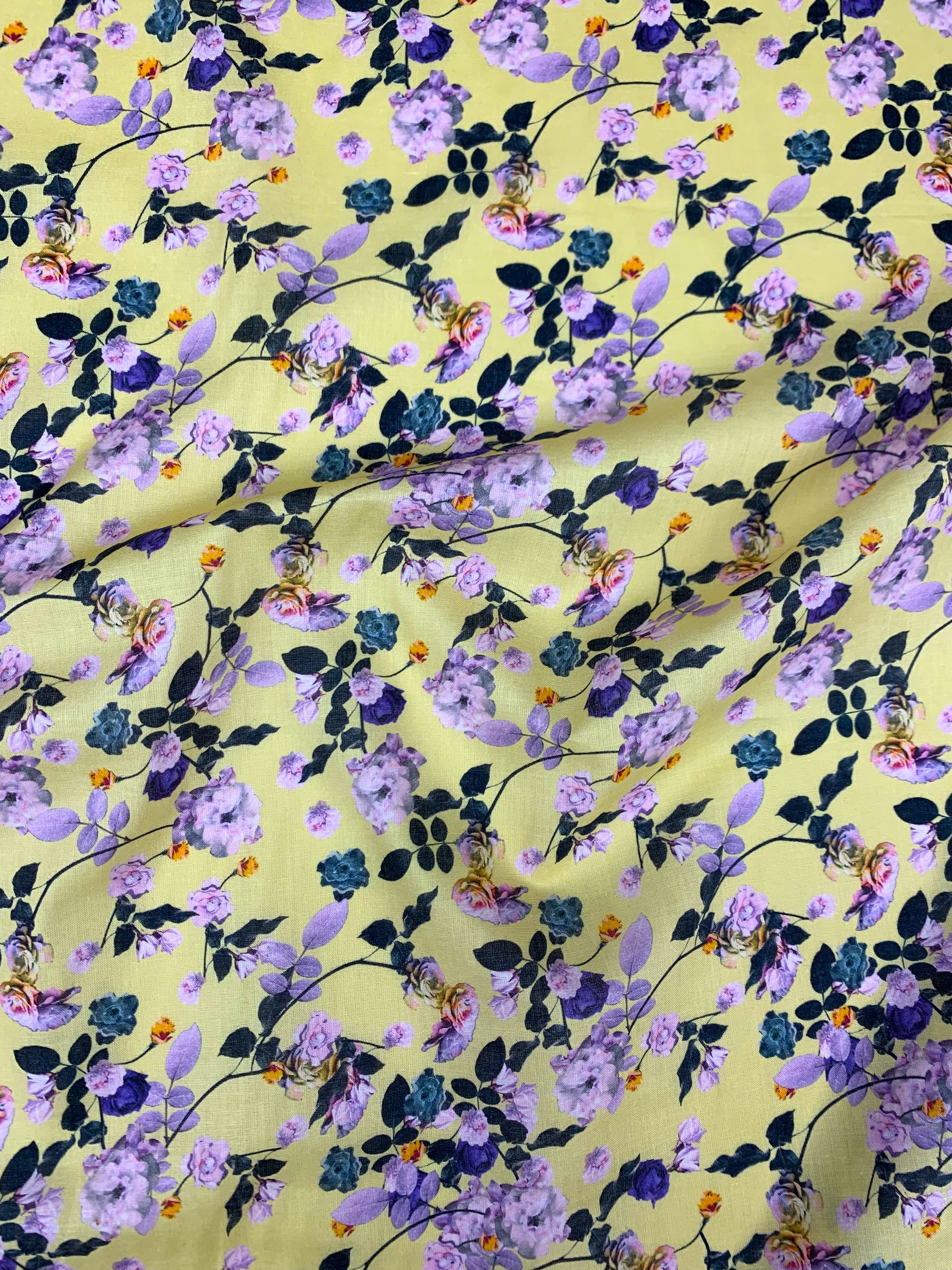  cotton lawn with purple and green flowers on a background of pastel yellow with a measuring tape on the bottom of the fabric.