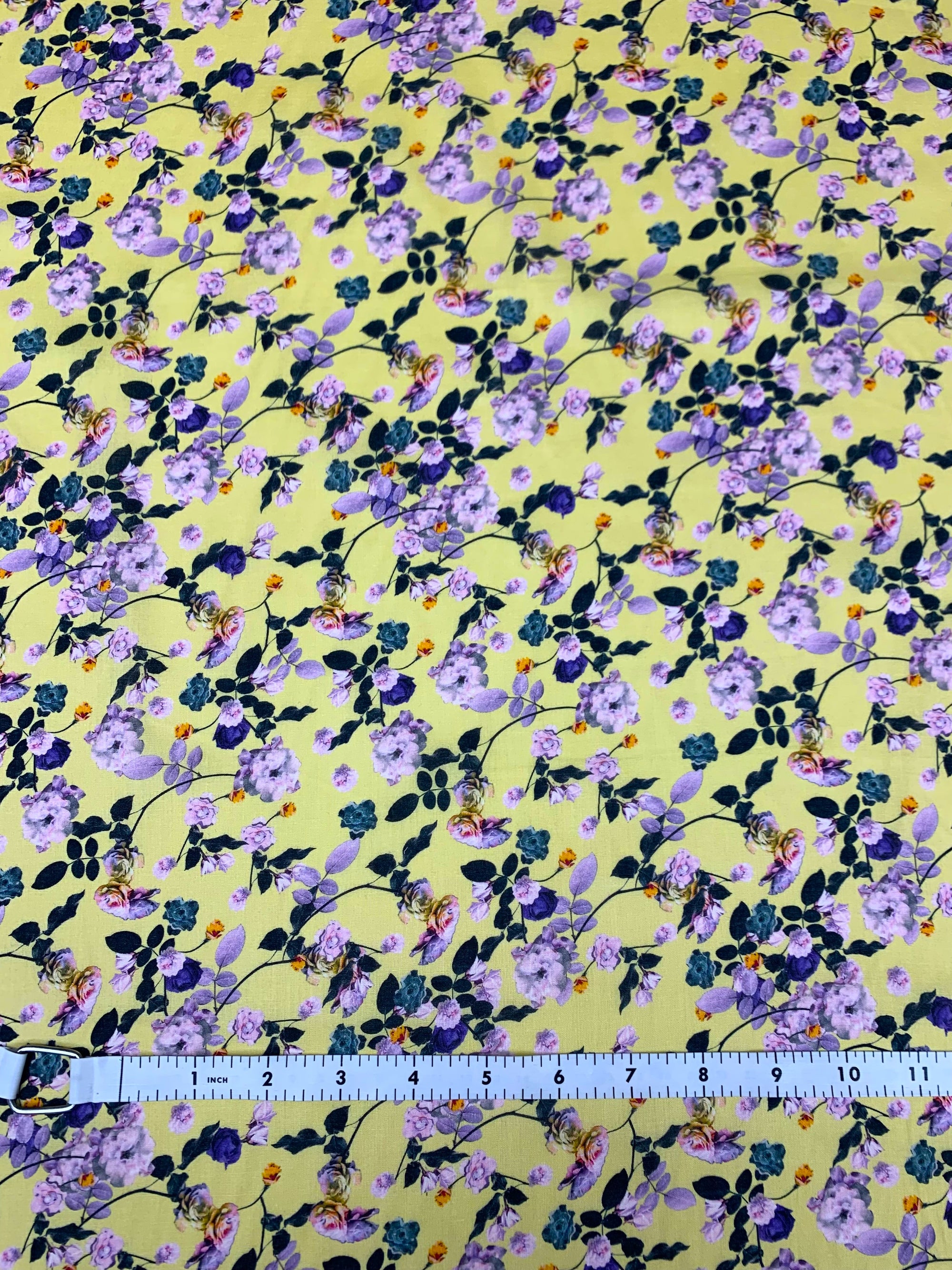  cotton lawn with purple and green flowers on a background of pastel yellow with a measuring tape on the bottom of the fabric.