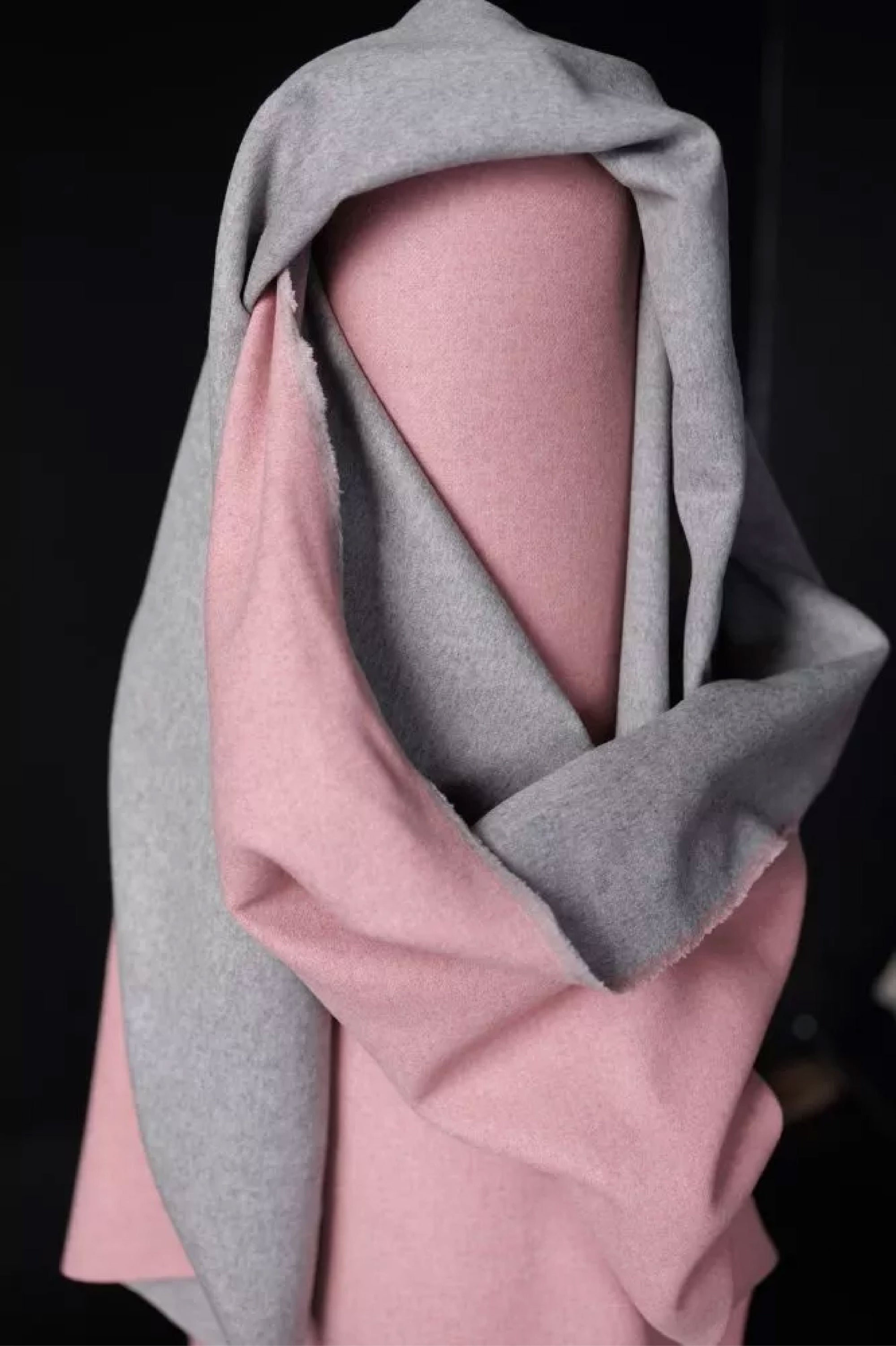 A roll of A soft and bouncy two toned wool in bright bubblegum pink on one side and grey marl on the other. On a Black background.