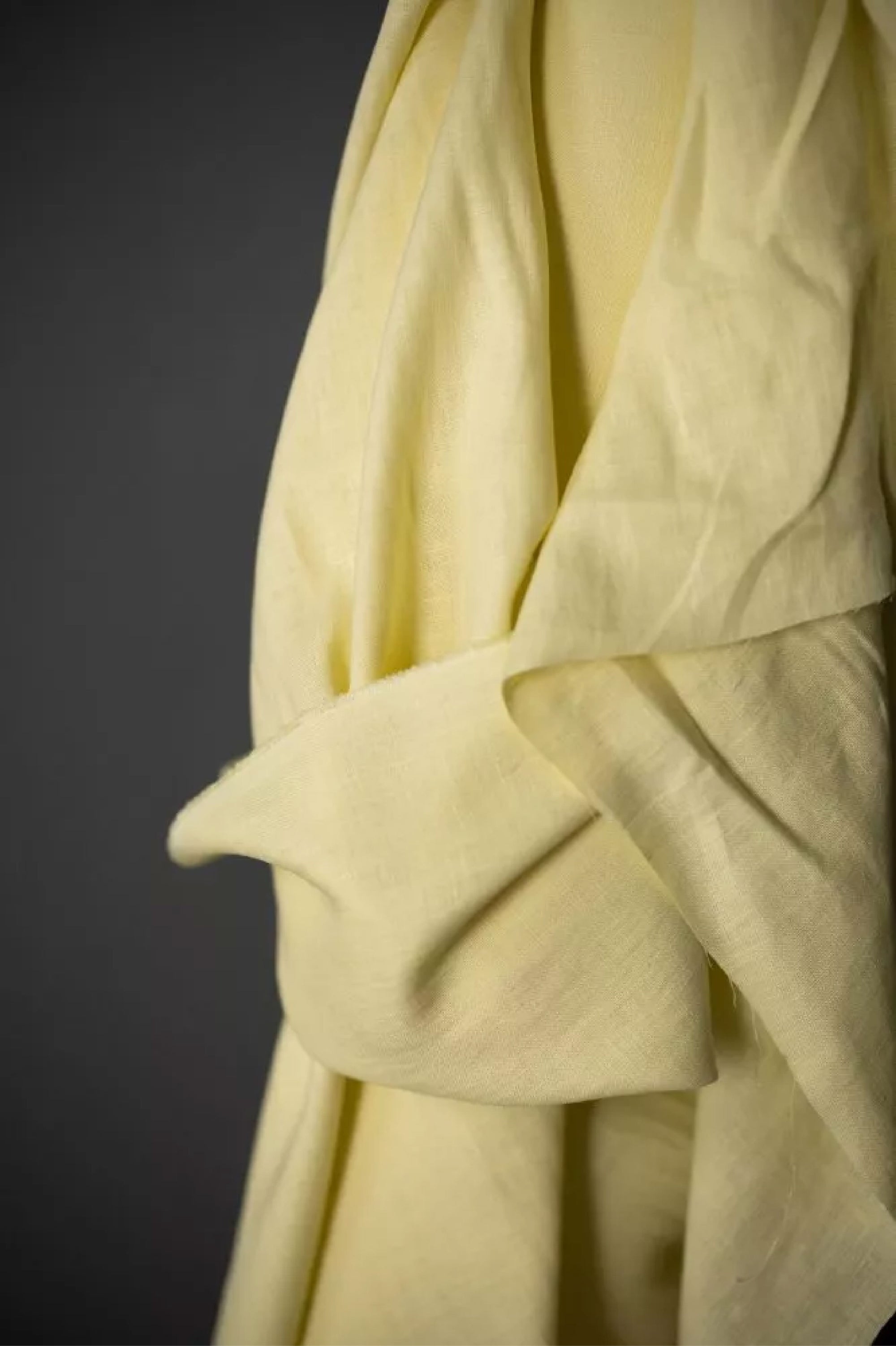 roll of  European laundered linen, tumbled at the mill for softness. Very pale yellow on a dark grey background.