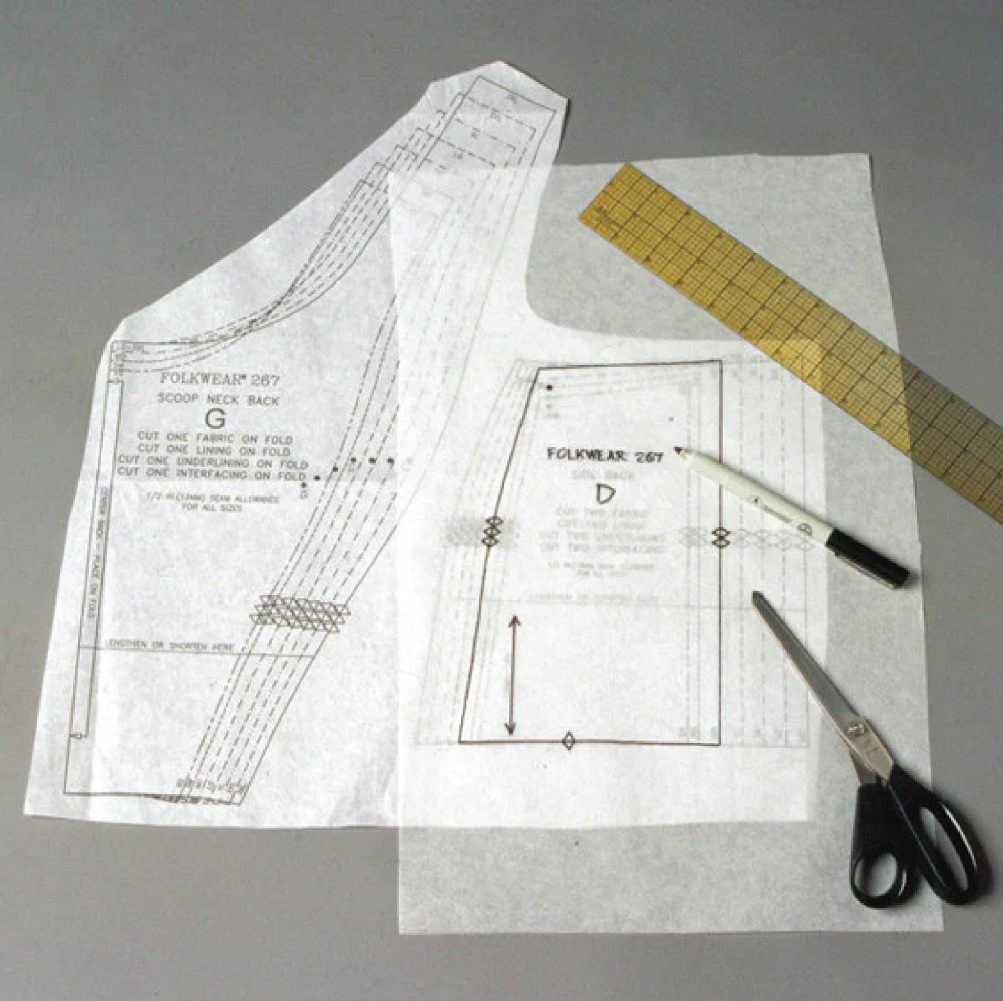 Tracing fabric on top of a sewing pattern along with scissors, a pen, and a ruler. 