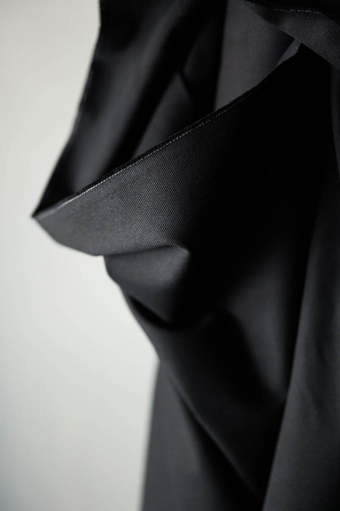 Black cotton canvas fabric standing up against a off white background.
