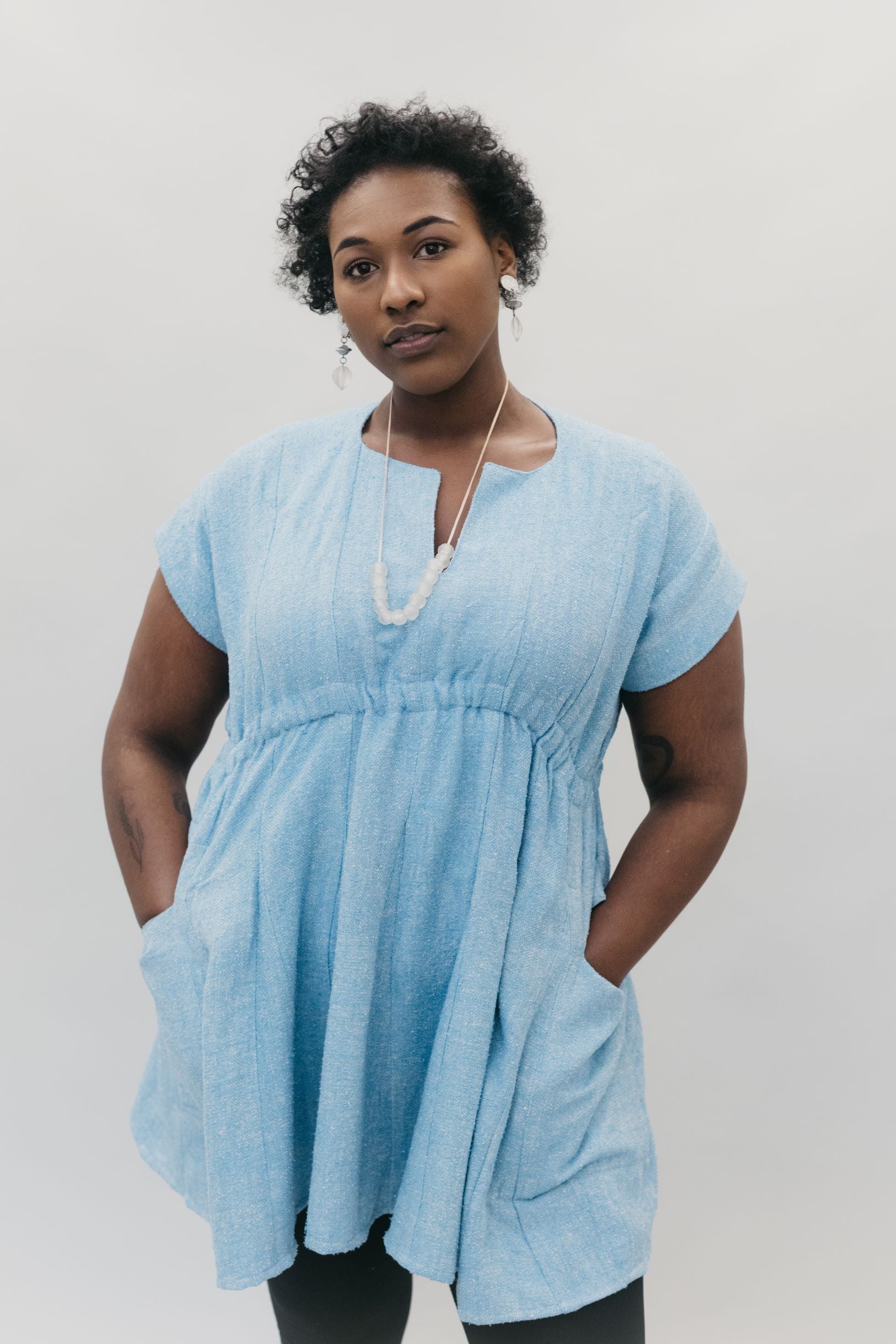 African American woman wearing the women's Ghanaian Smock in light blue with hands in pockets. 