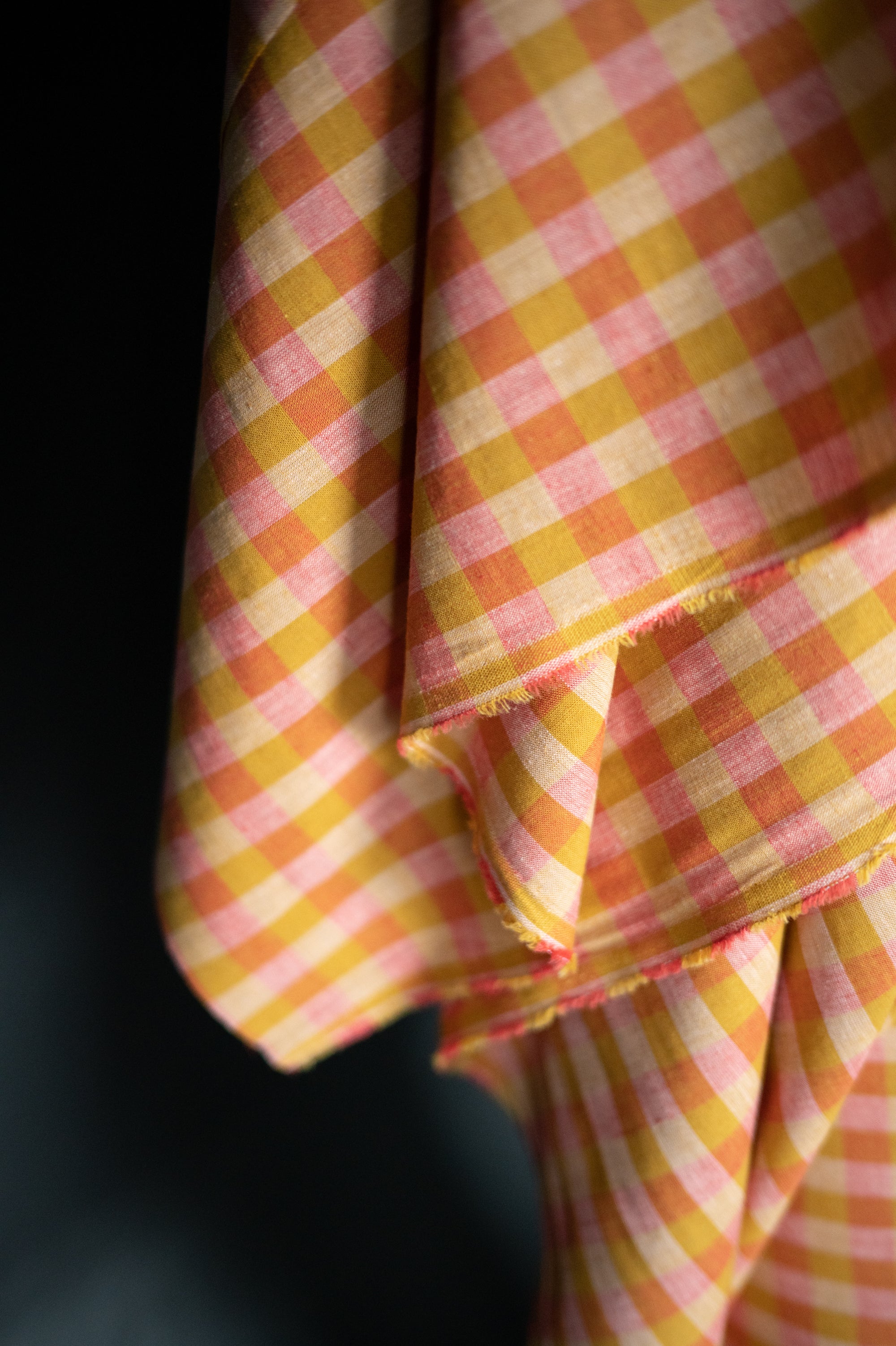 close up of A soft cotton and linen blend in a cheery check of raspberry pink and mustard yellow. A versatile cloth that is a great alternative to linen.