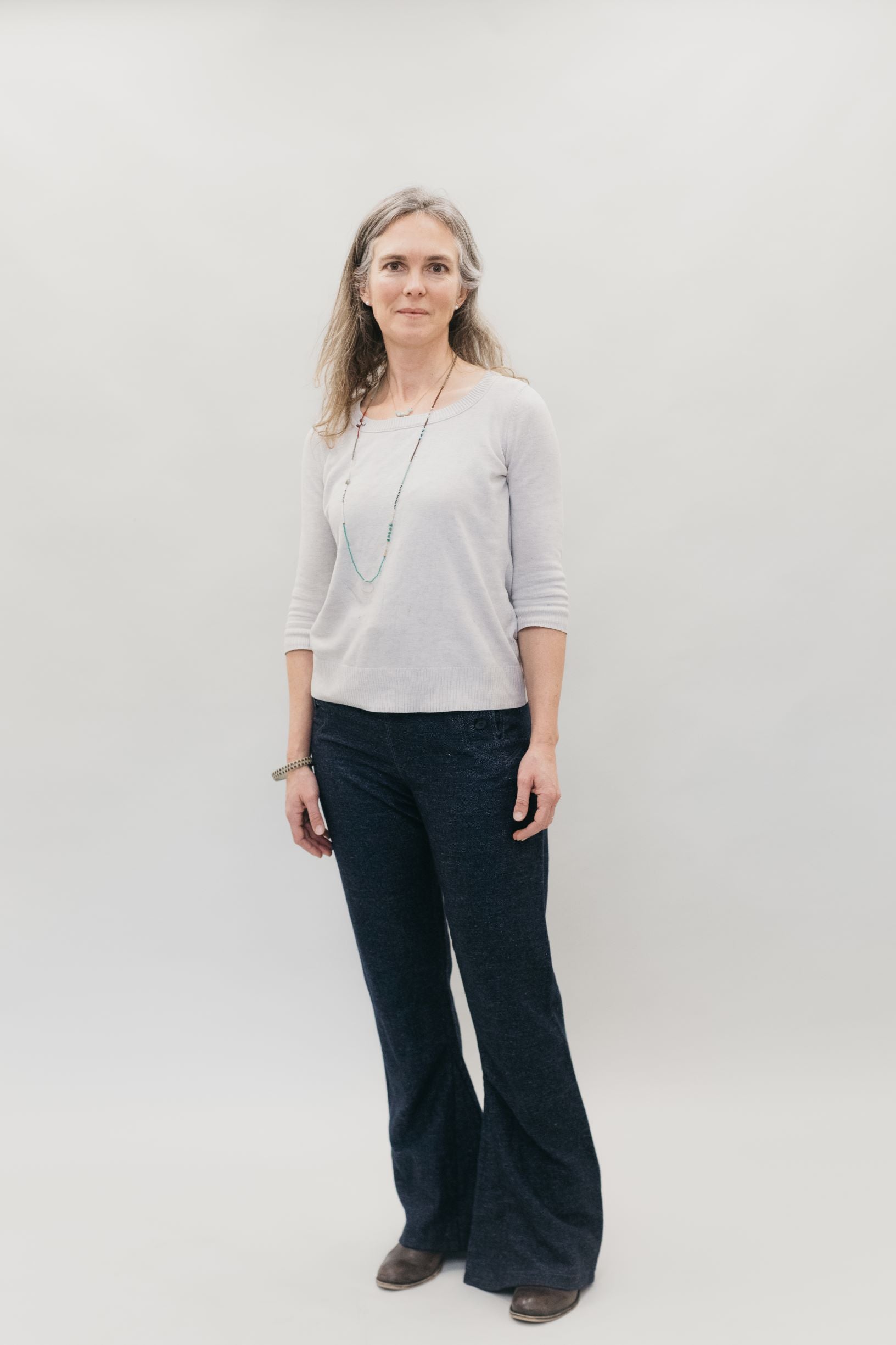 Woman standing in front of a white back ground in navy sailor pants and white shirt.