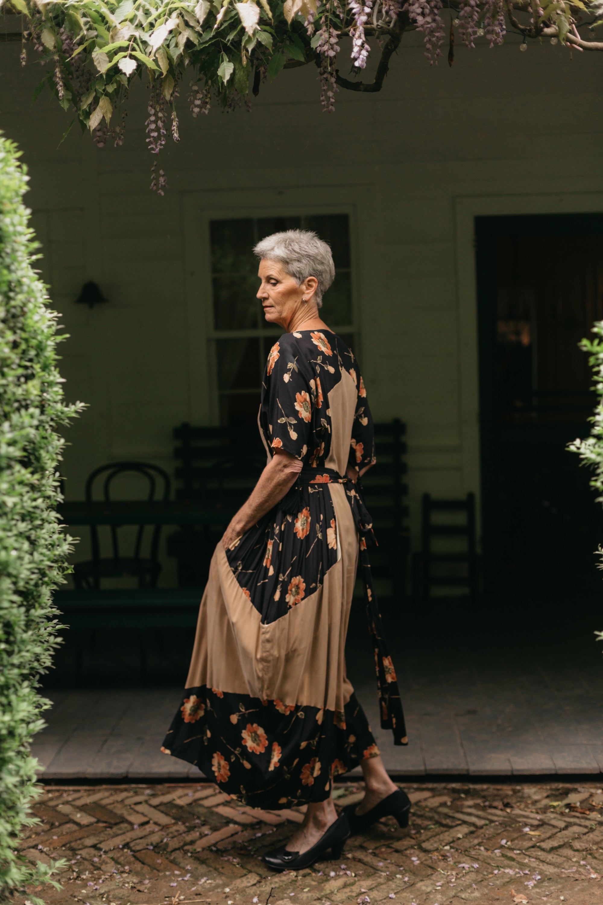 Older white woman outside twirling in a black and brown elbow length sleeve gown.