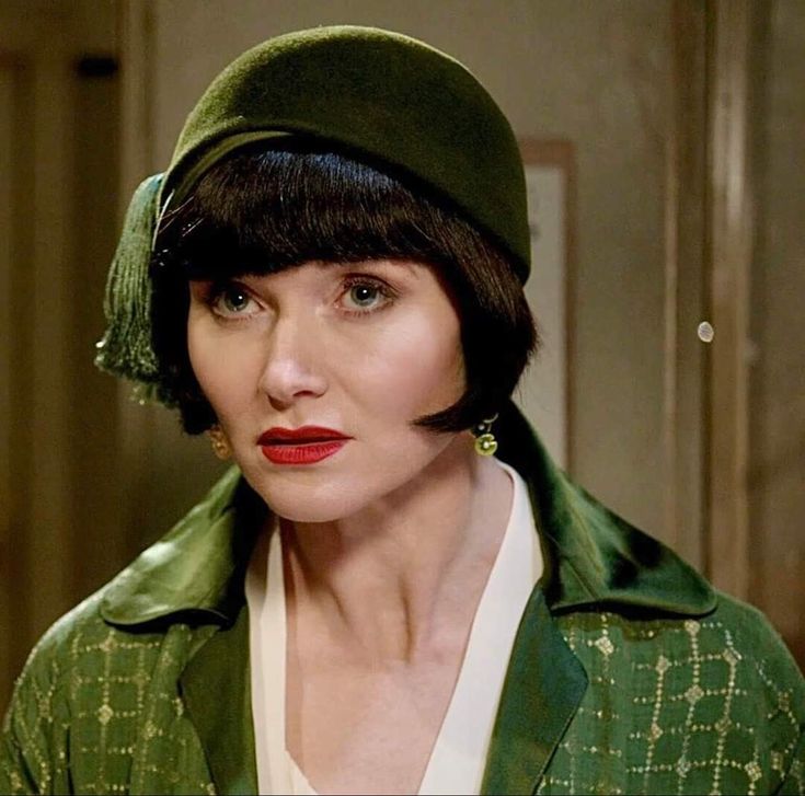 Headshot of Miss Fisher in a green cloche hat and a green coat