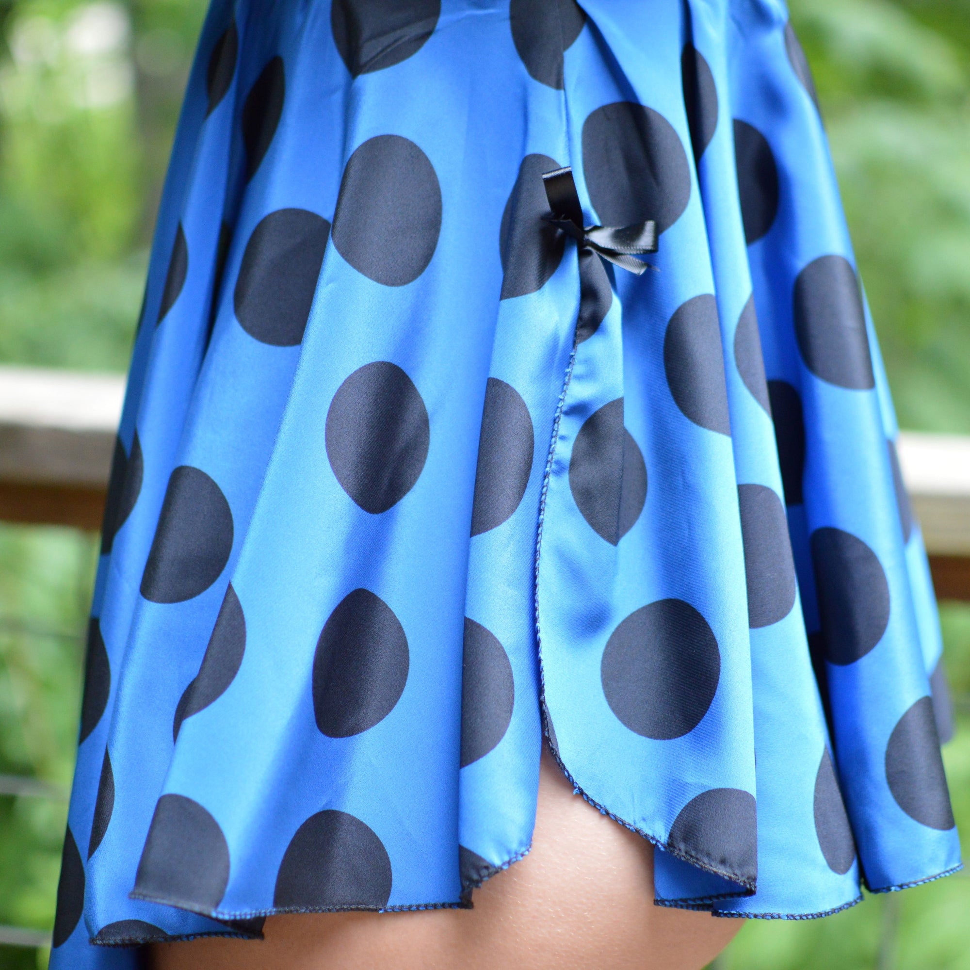 Young woman standing outside with her back to the camera, wearing a blue lingerie top with black polka dots and black straps.