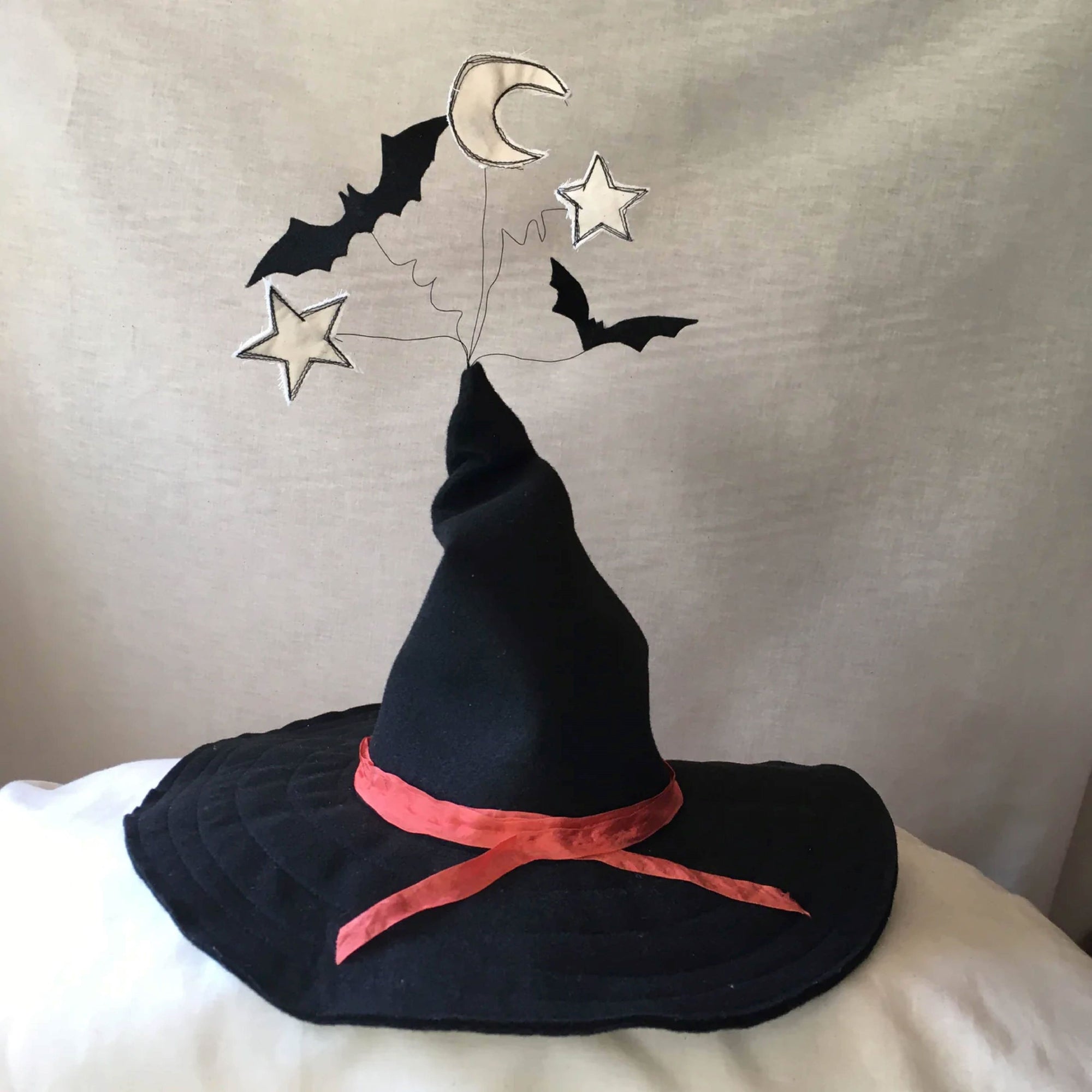 Black witches hat with an orange ribbon on brim and felt bat with stars and moon sticking out of the top on wires.