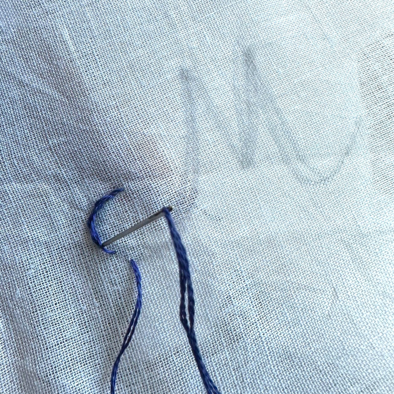Starting a monogram on white fabric with blue thread.  letter M