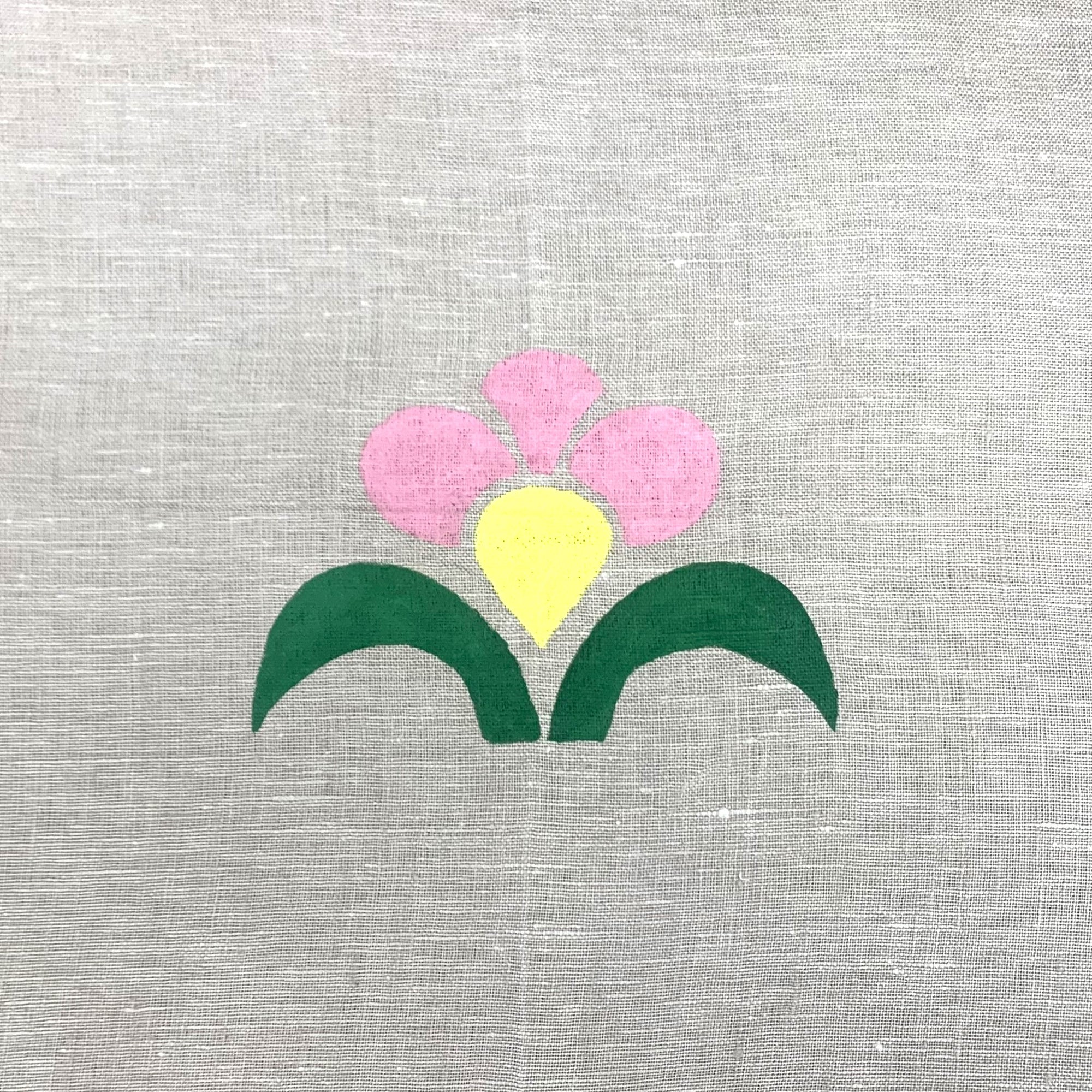 Painted pink flower with a yellow bud and green leaves using a stencil on beige linen fabric.
