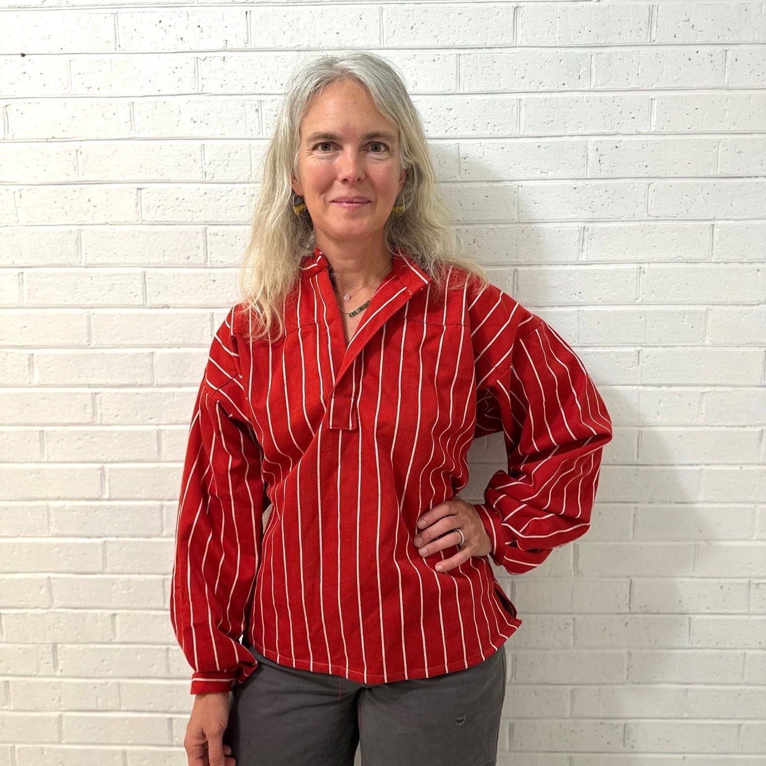 Woman wearing a red striped busserull in front of a white brick wall.