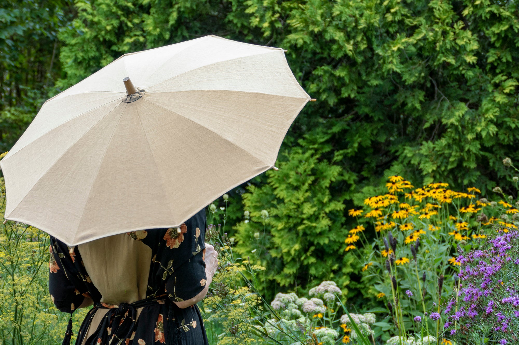 Woman standing in a garden holding a parasol with her back to the camera