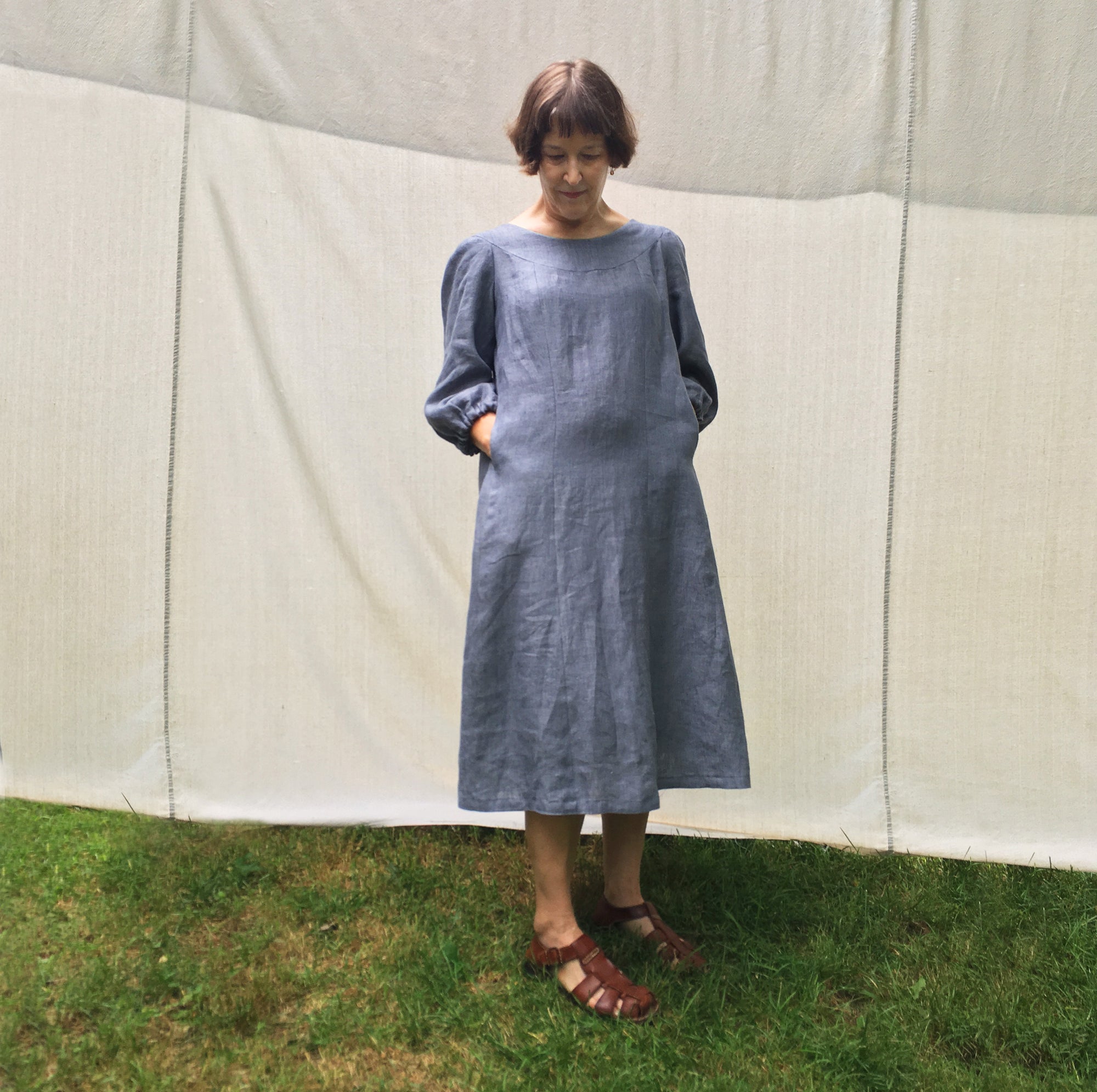 white woman with short hair stands in front of light fabric background in midi length dress with long sleeves mu'umu'u muu-muu moo-moo dress sewing pattern