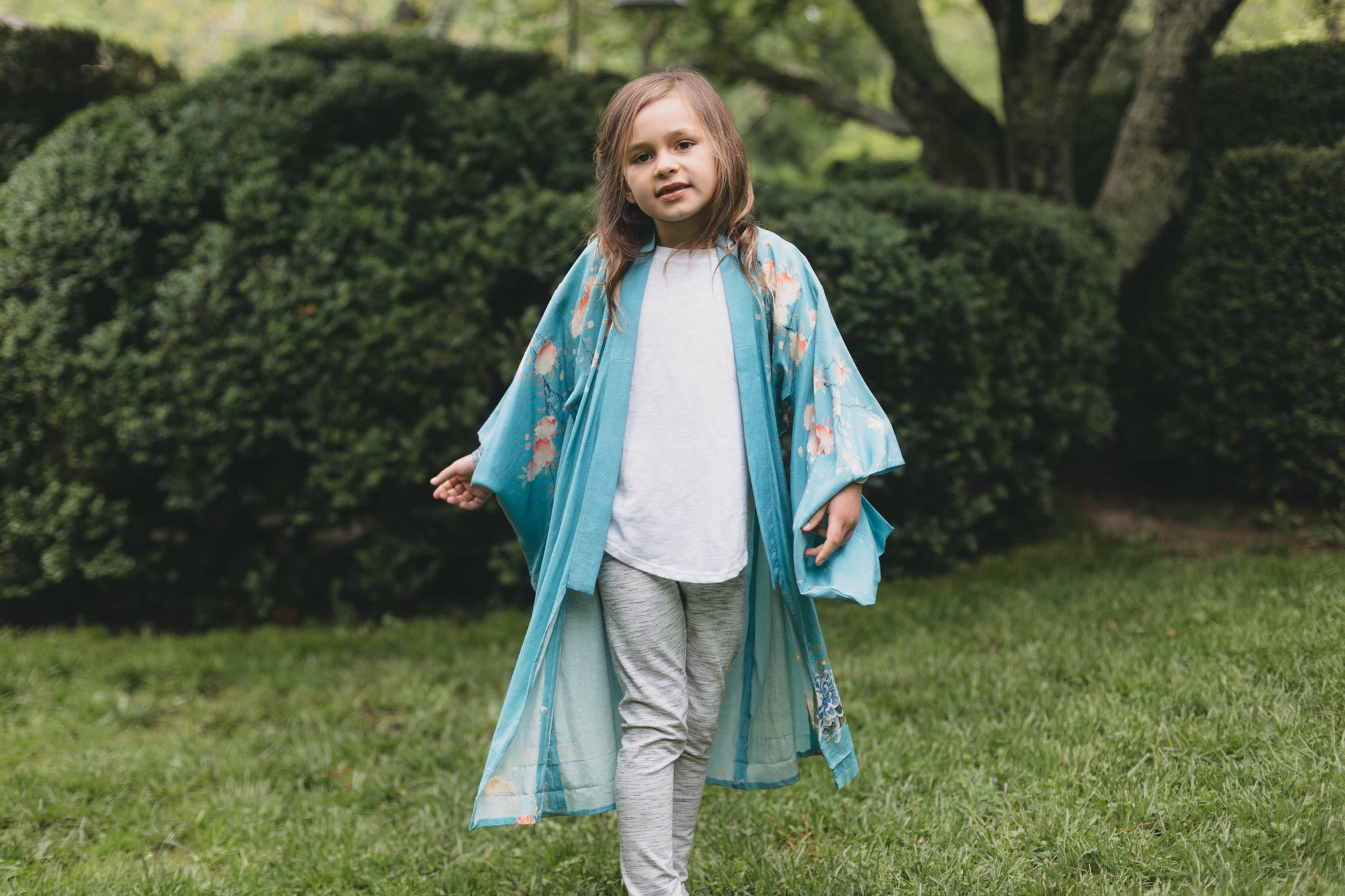 Child wearing a blue floral kimono standing in a garden
