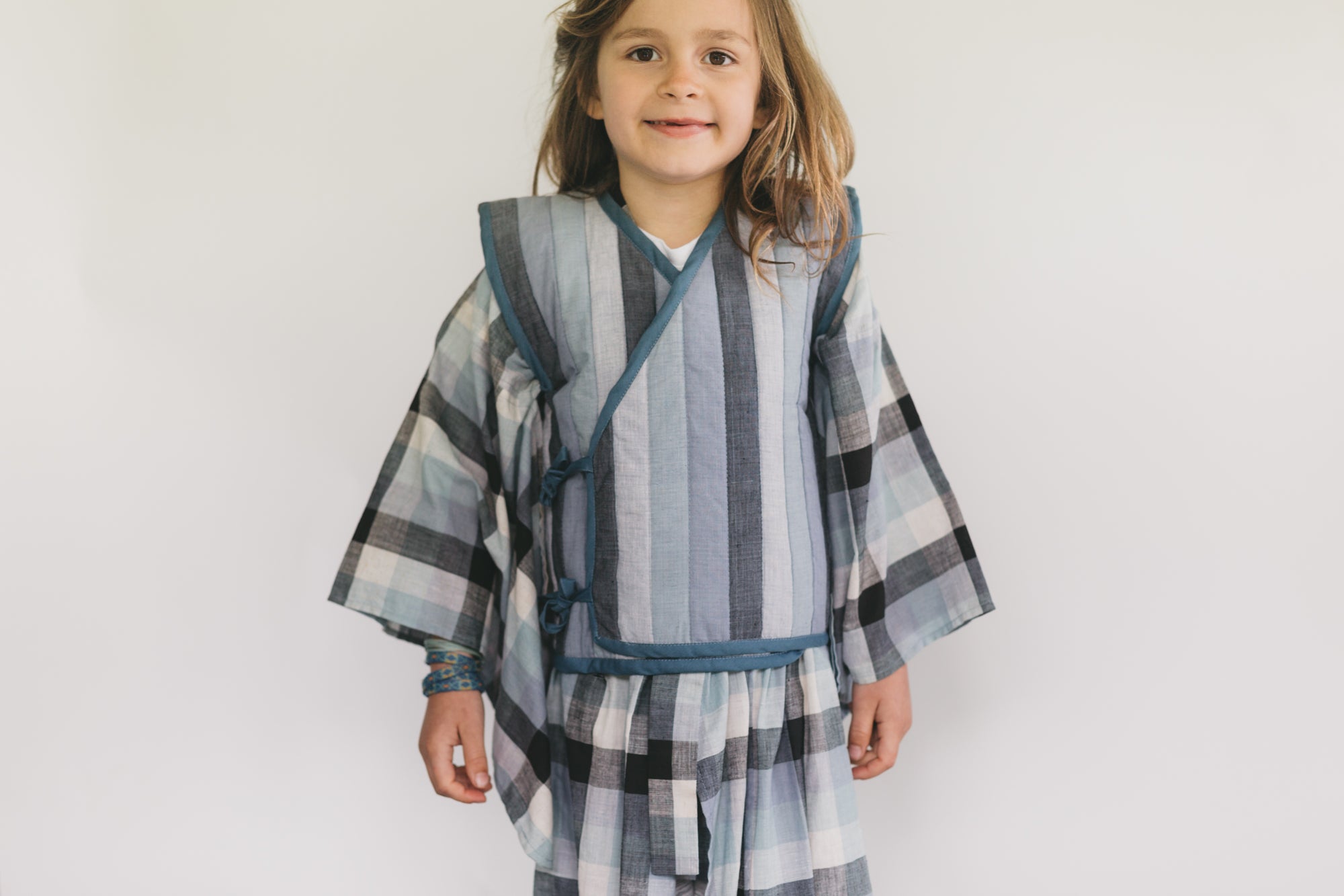 Child wearing a striped Kimono and vest against a white background
