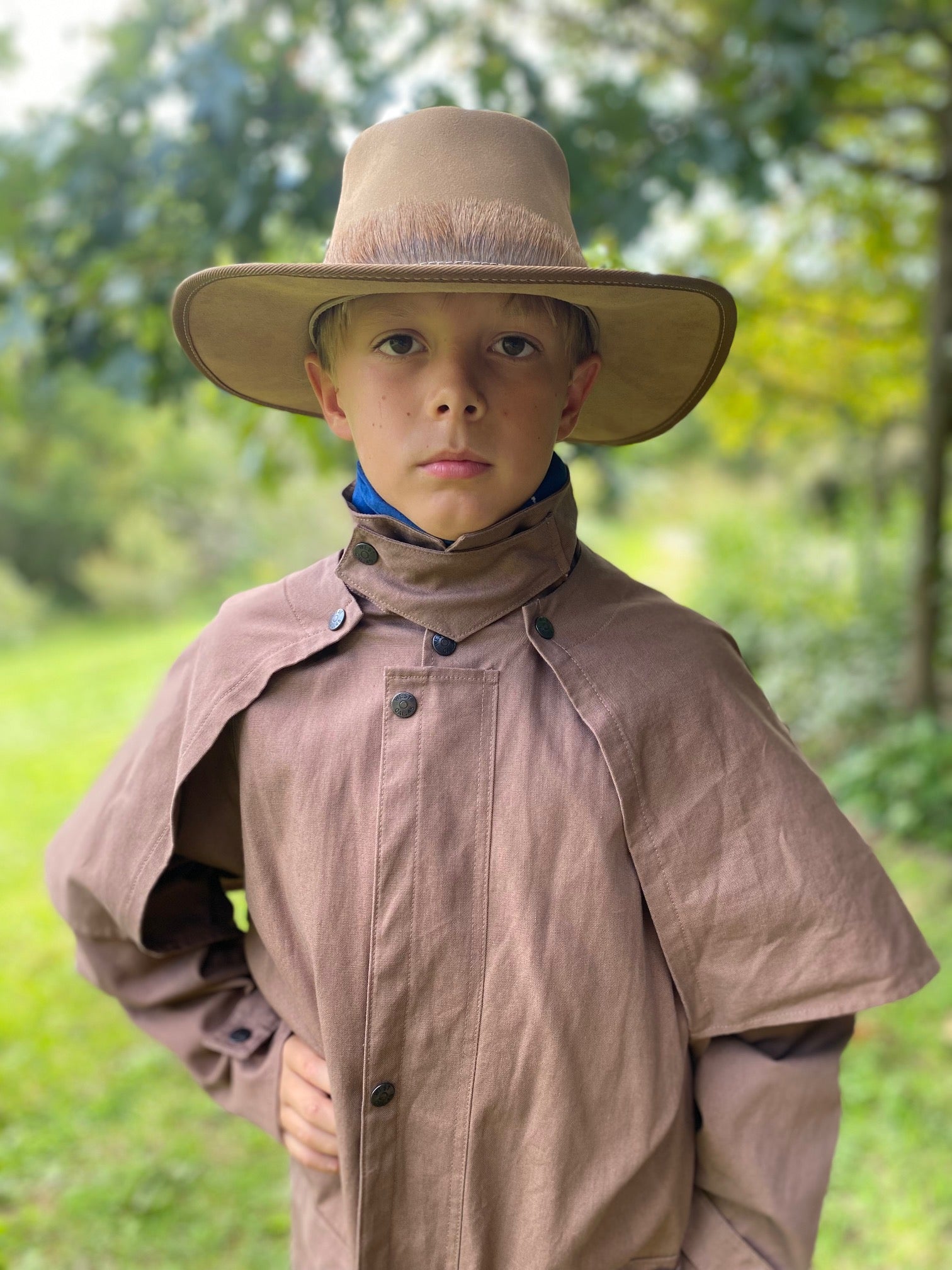 Boy wearing a brown drovers coat and a cowboy hat with his hand on his hip.
