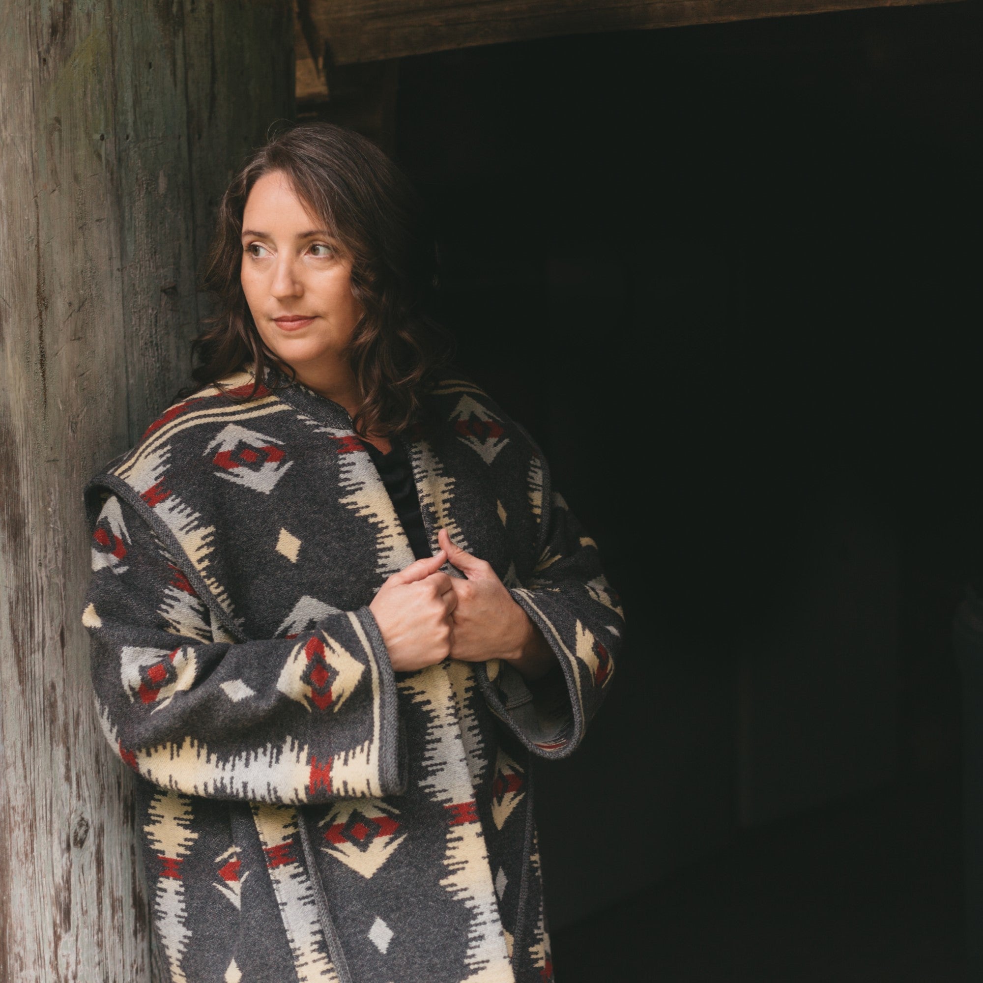 Woman leaning on a barn door in  patterned great szur coat.