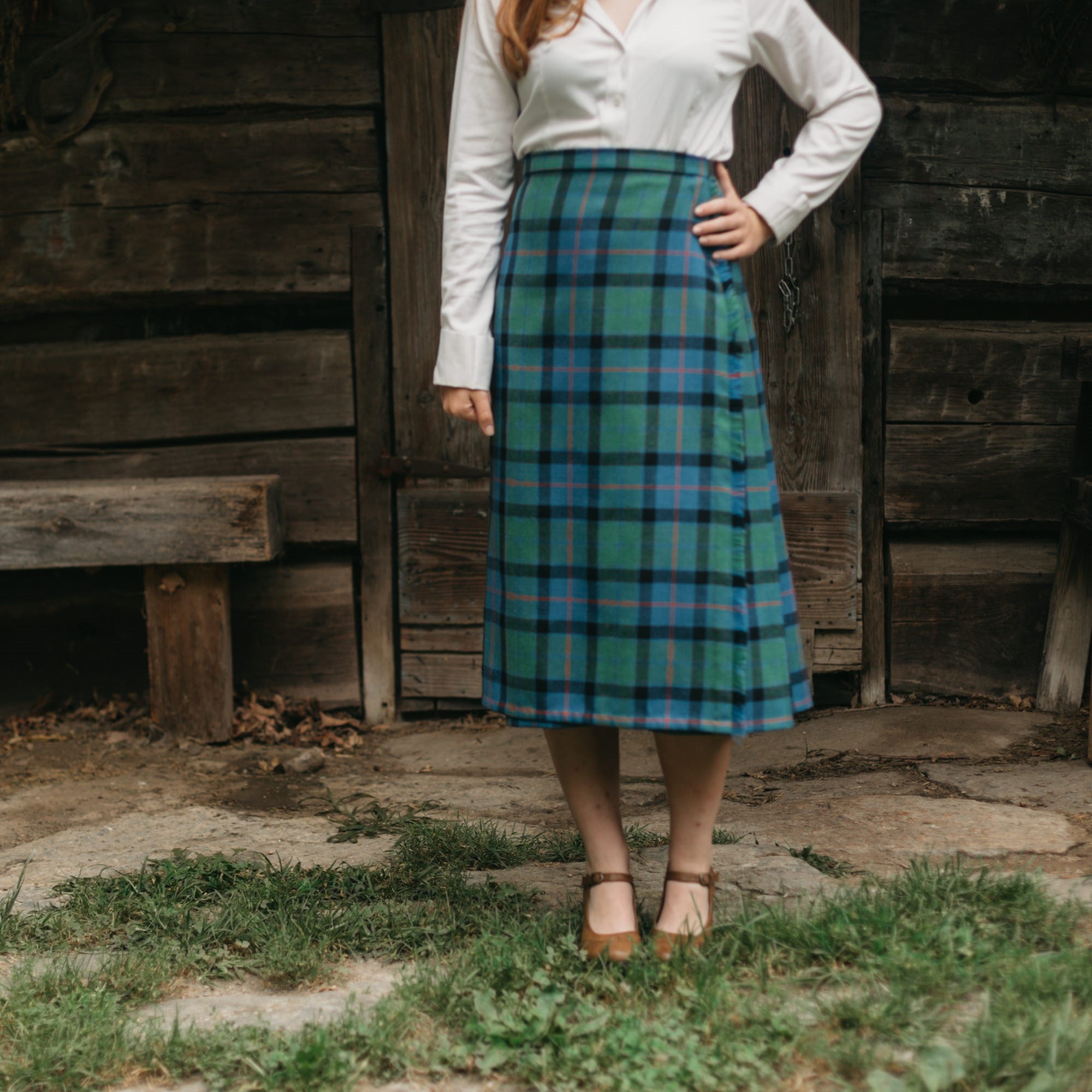 Close up of long woman's kilt worn outside with brown shoes and white top.