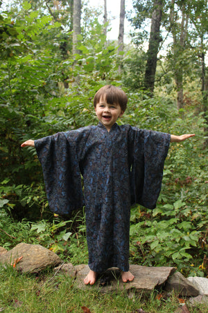 Boy standing outdoors in a forest in  a dark blue kimono with trees and greenery in the background