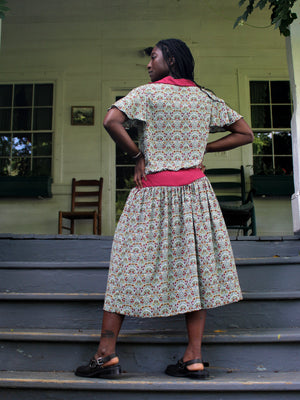 Woman standing on outdoor stairs wearing a vintage tea frock, back to camera, hands on hips