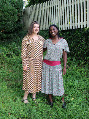 Two women in a field wearing vintage patterned tea frocks.  Woman on right has short sleeves, woman on left has long sleeves