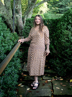 Woman by bushes wearing a long sleeved patterned tea frock