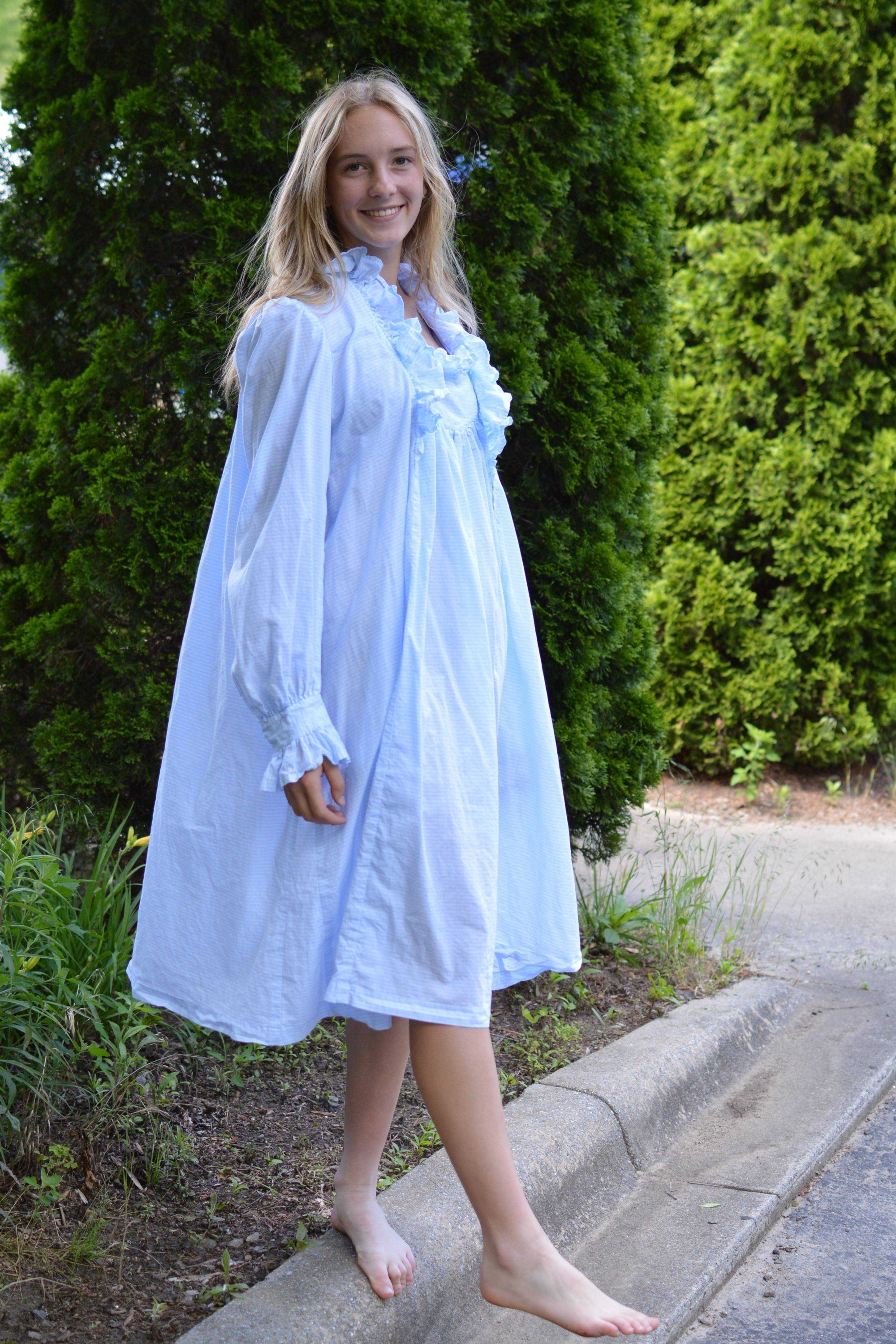Young woman standing on a curb in a light blue ruffled nightgown.