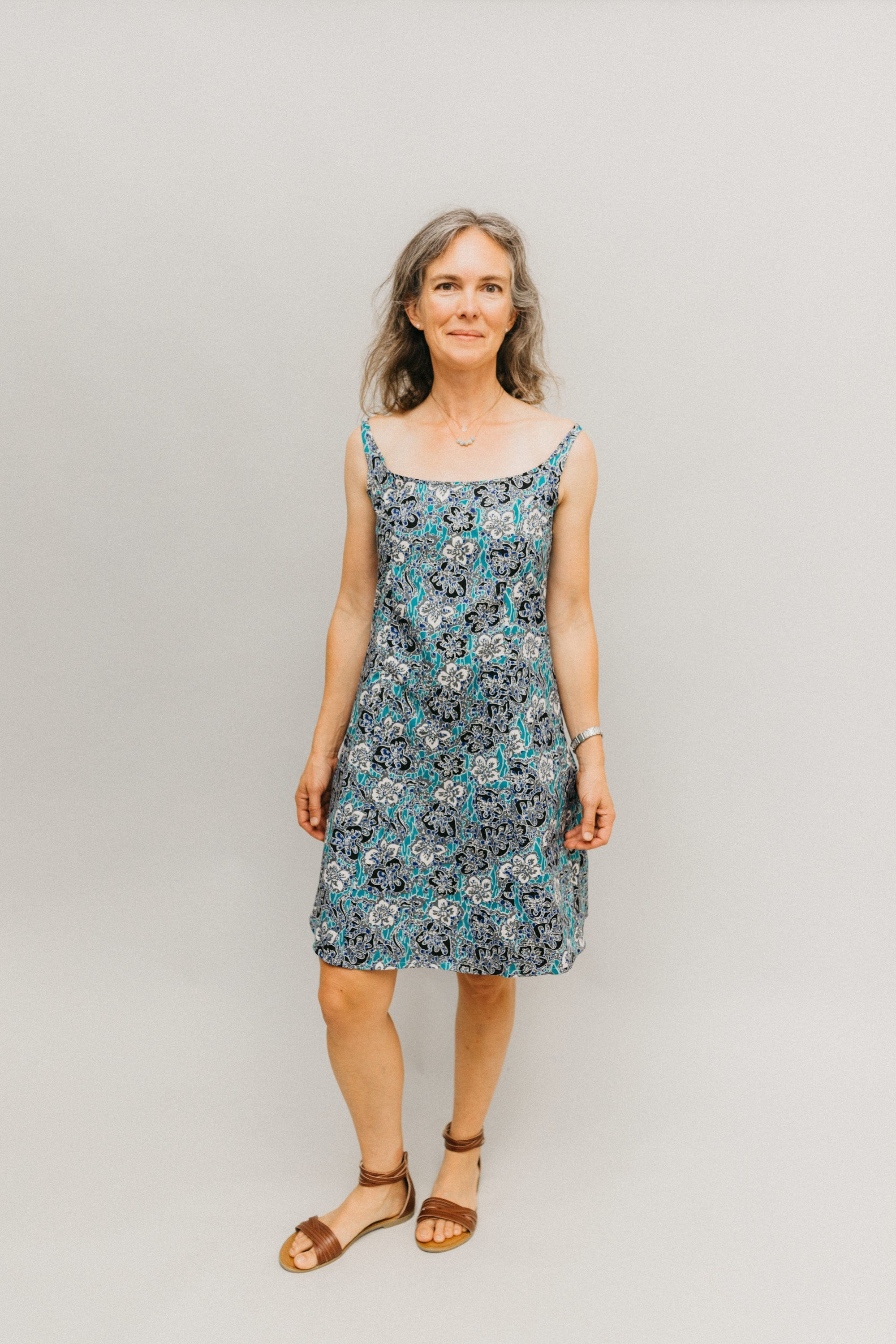 Woman wearing a teal, white, and black floral knee-length dress with narrow straps.