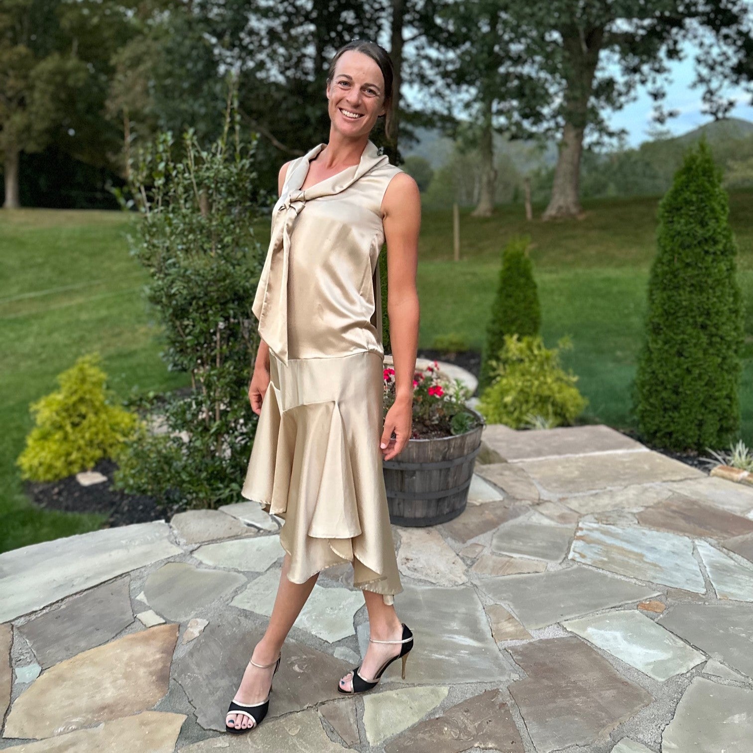 Woman standing on a patio outside wearing a gold tango dress and black and gold heels.