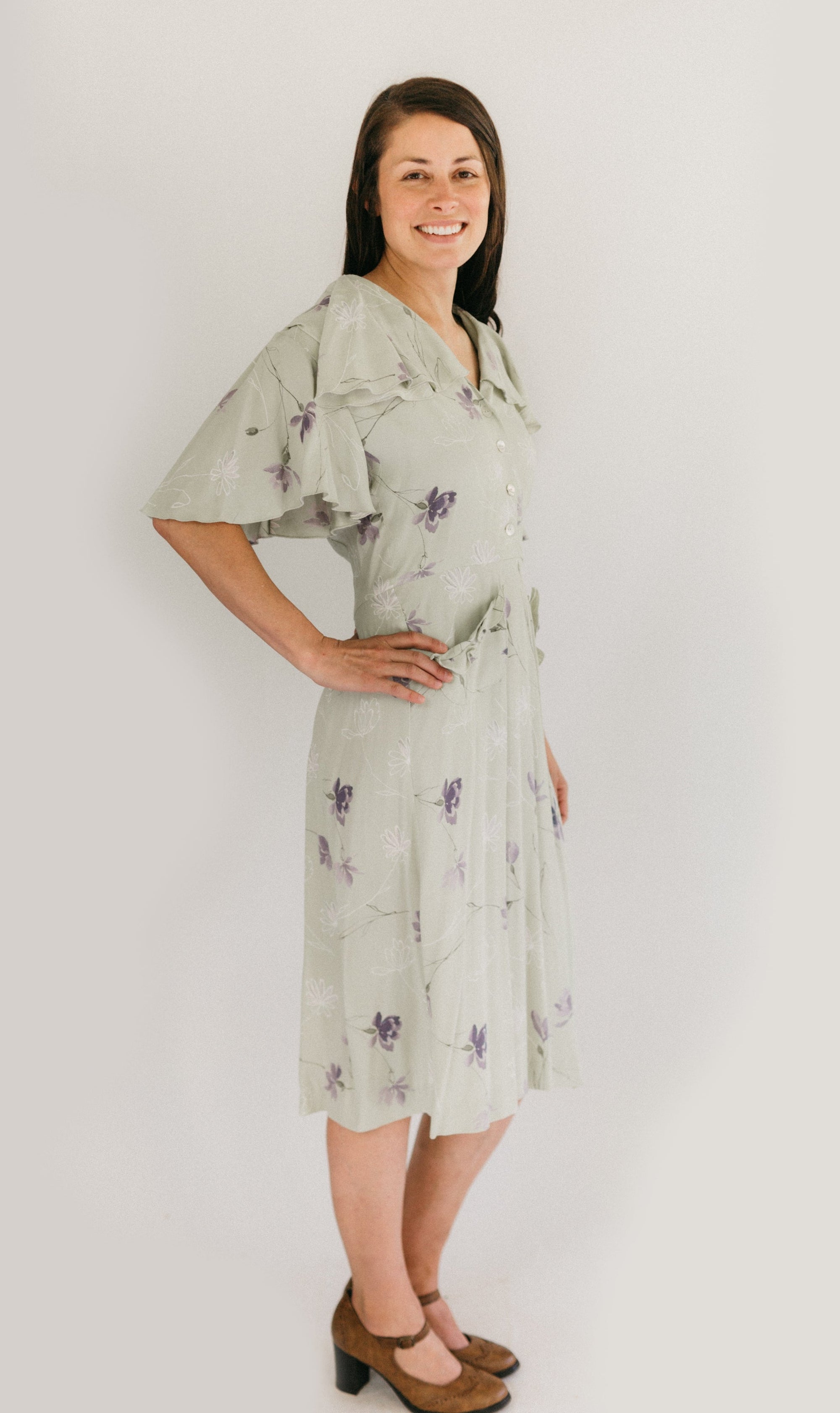 Woman wearing the view B in a light mint green and lavender floral. View B is more casual, with buttoned front, flounce collar and sleeves, and eyelash pockets.