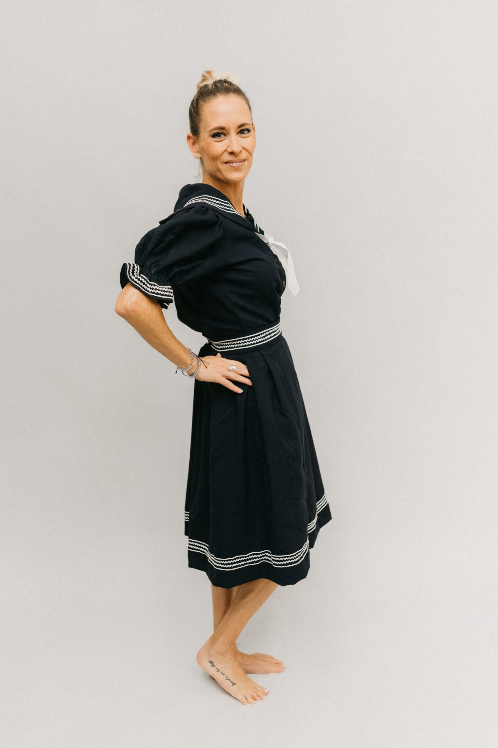 Side view of blonde white woman with hands on her hips standing in front of a white studio backdrop knee bent wearing the 253 Vintage Bathing Costume.