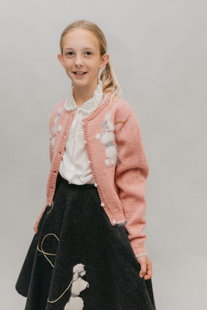 Young blonde girl smiling and standing in front of a white studio backdrop, wearing #256 At The Hop skirt, blouse and sweater.