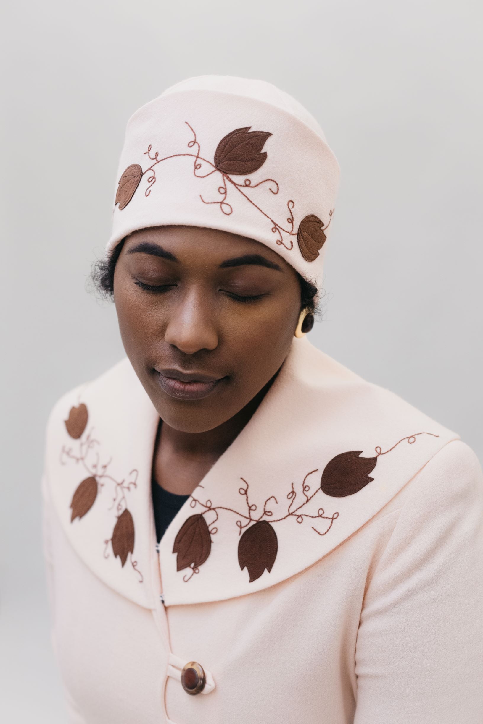 Black woman wearing a pink wool cloche hat with brown feather applique and embroidery on it.