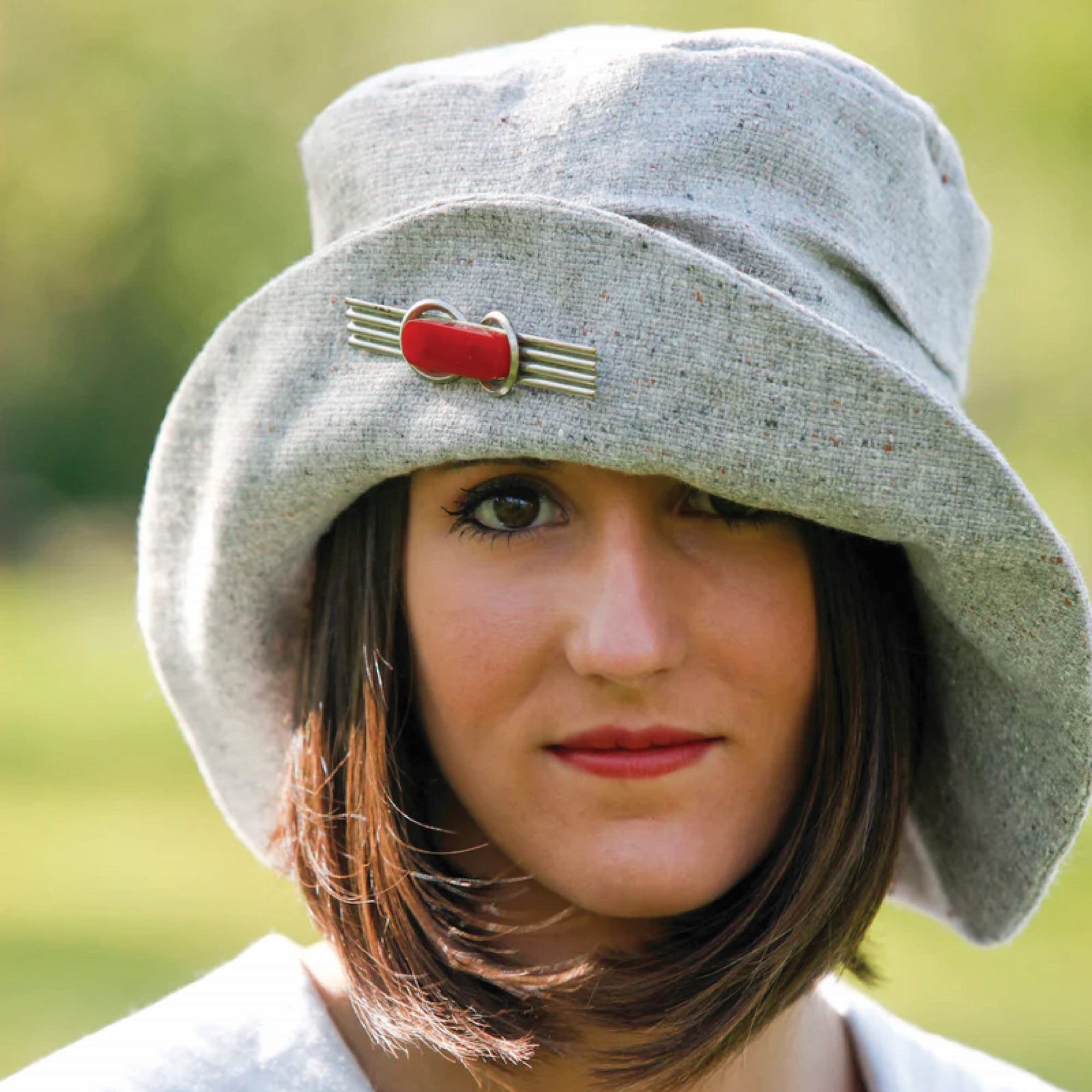 Woman's face and head in a grey slouchy hat with a red brooch.
