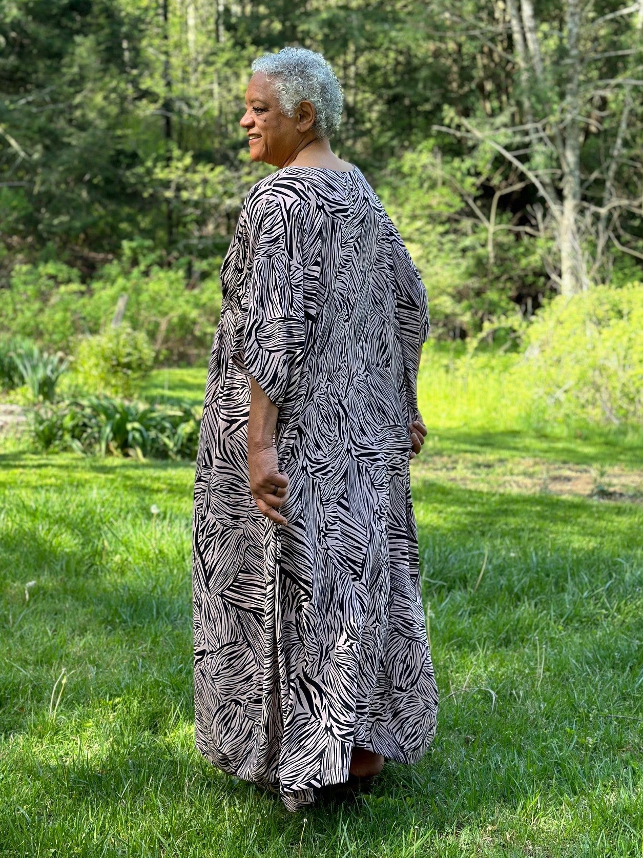 Woman standing outside wearing a pink and black patterned kaftan.  Her back is toward the camera.