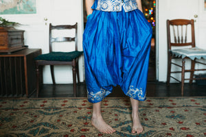 Person wearing blue harem pants from the Algerian Suit with white patterns in a room with chairs and a rug.