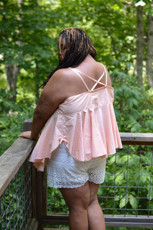 Woman with back toward the camera wearing a cross back peach lingerie dress with white lace bloomers.