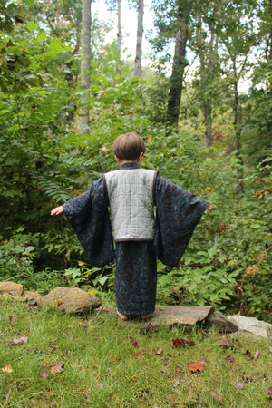 Boy with back to camera standing in a forest with trees and greenery in the background
