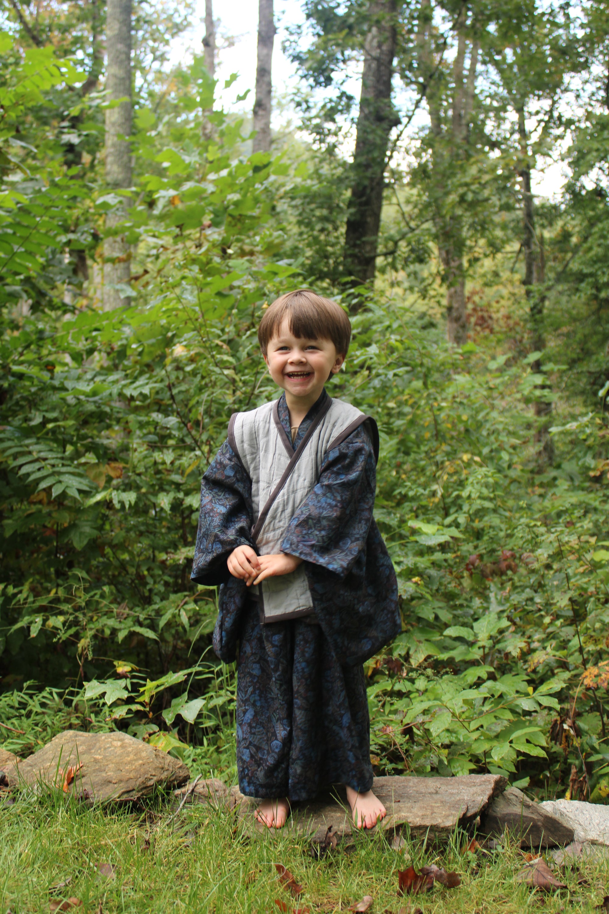 Child standing in a forest with greenery and trees in the background