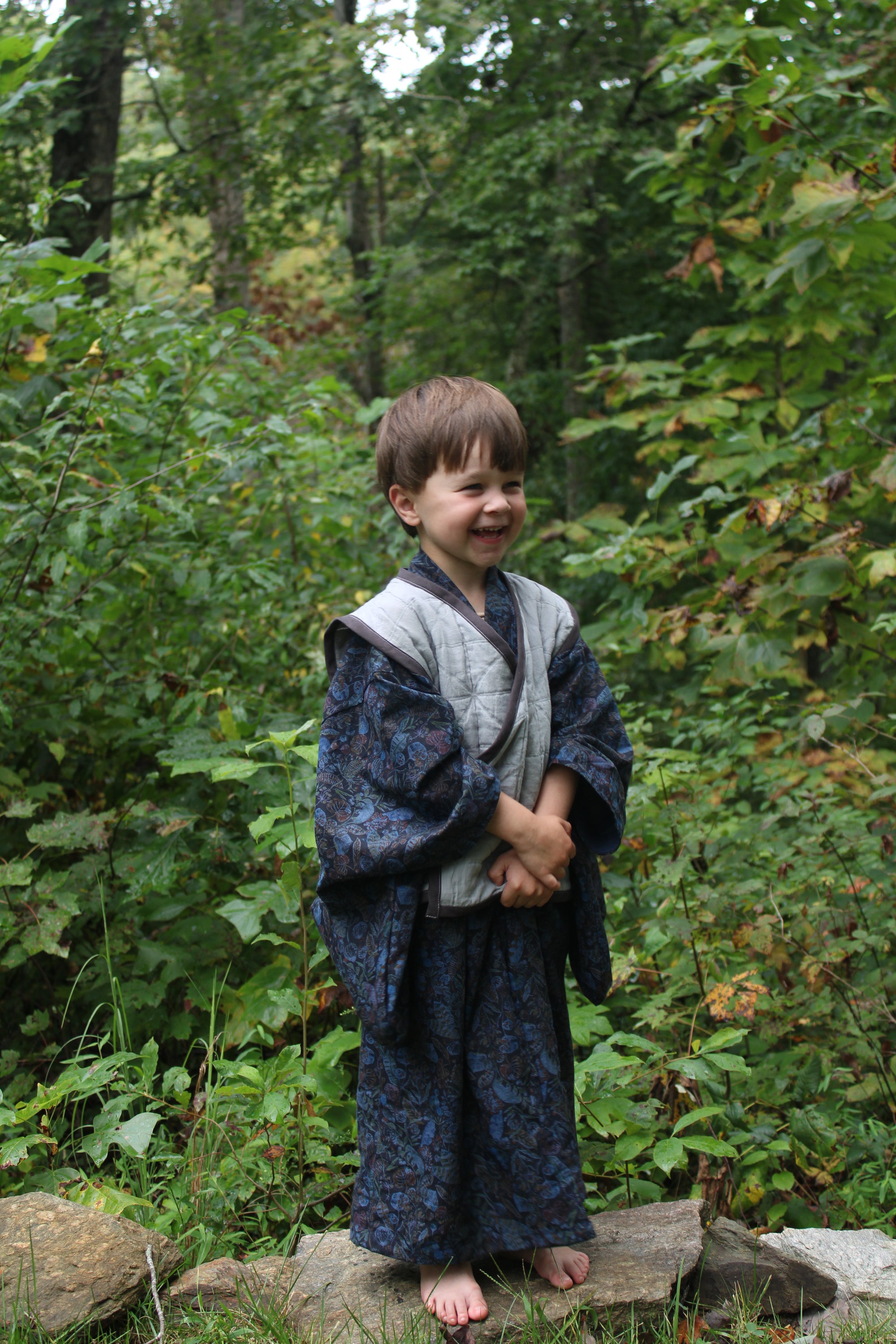 Child in a forest wearing a dark kimono coat with a grey vest