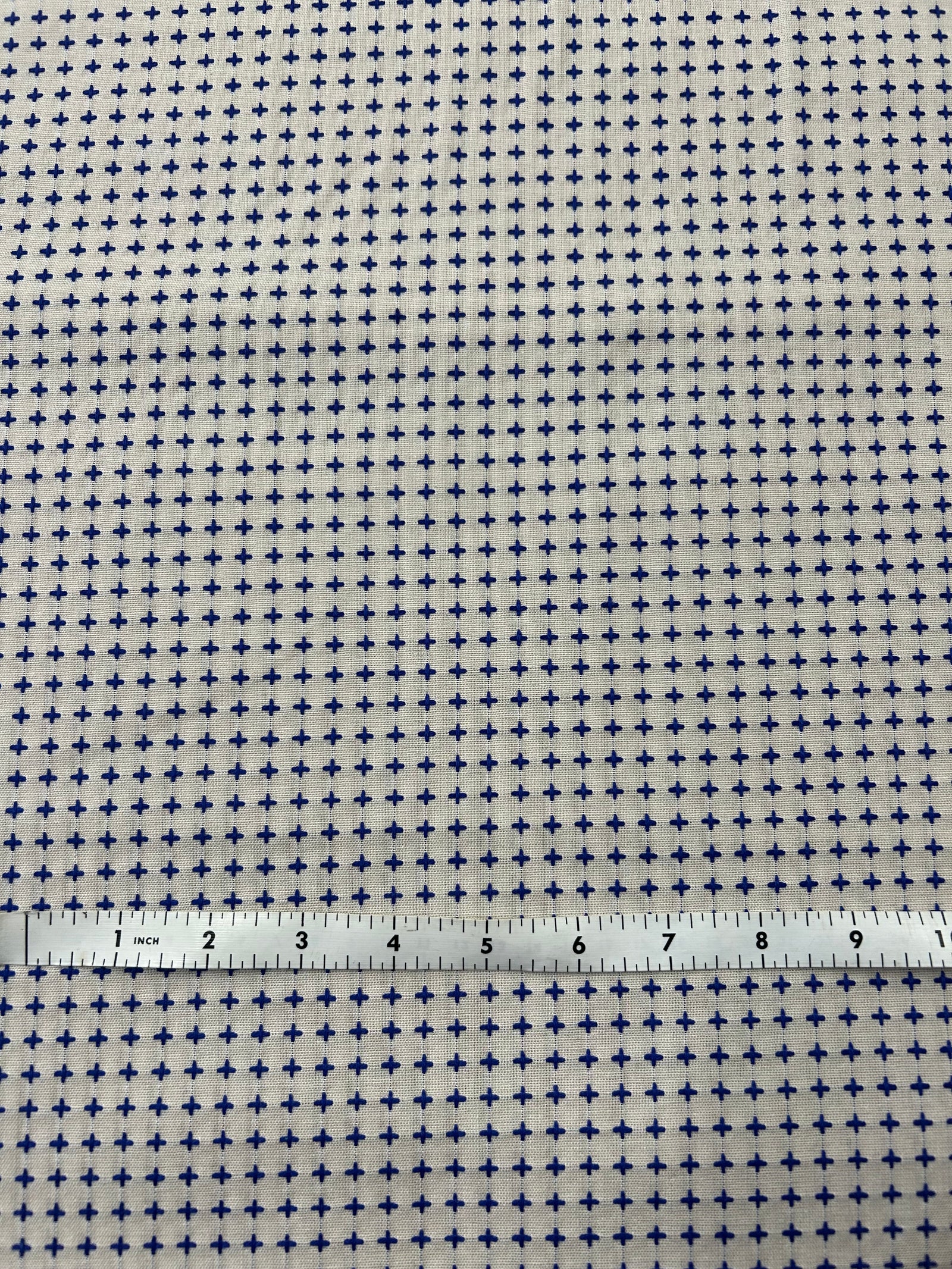 Fabric with a small cross pattern and a ruler for scale on a white background