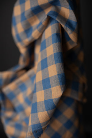 Close up of fabric in a sky blue and peach gingham with a very dark grey background.
